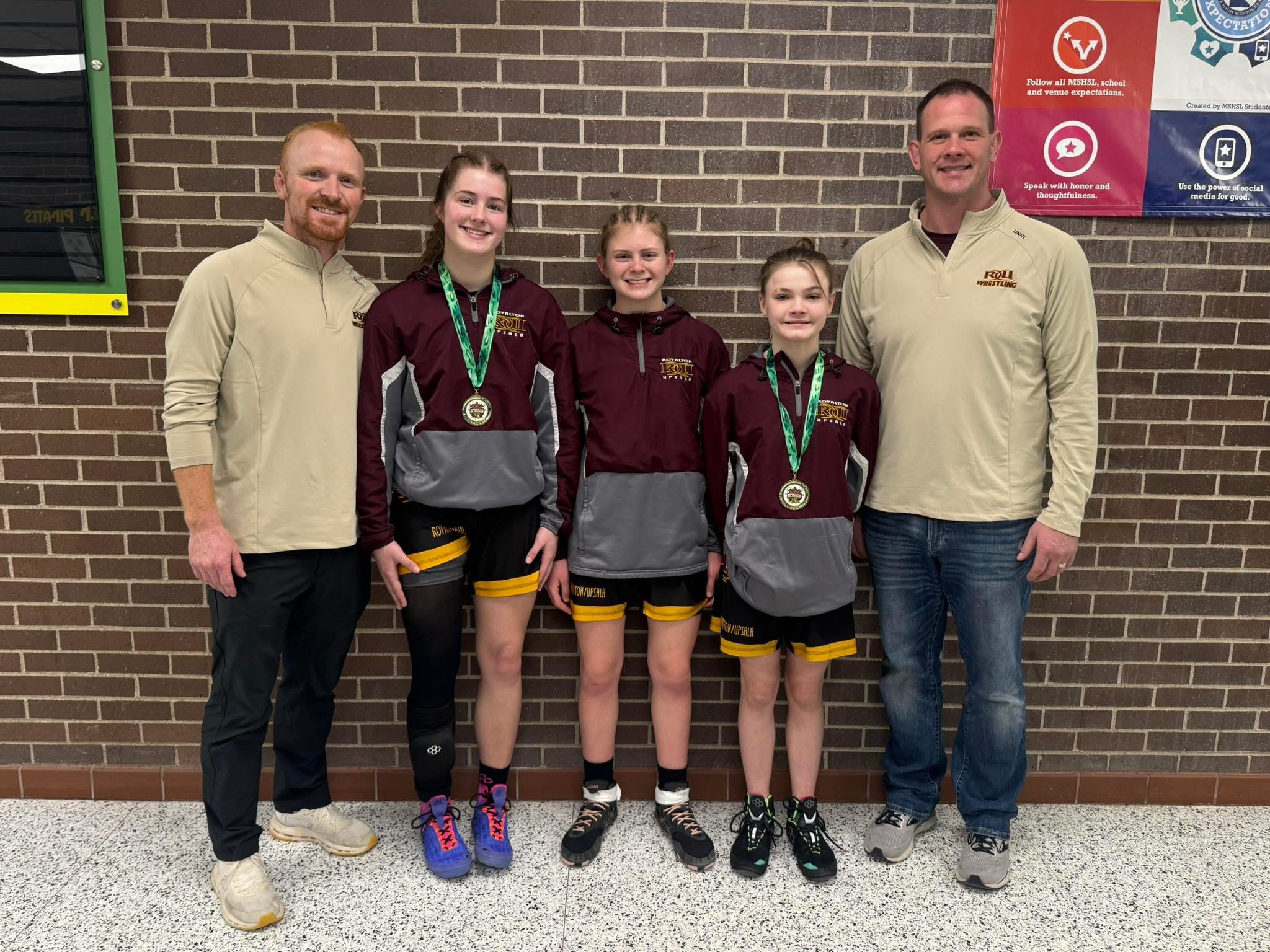 Three young athletes pose with two adults, all wearing medals.
