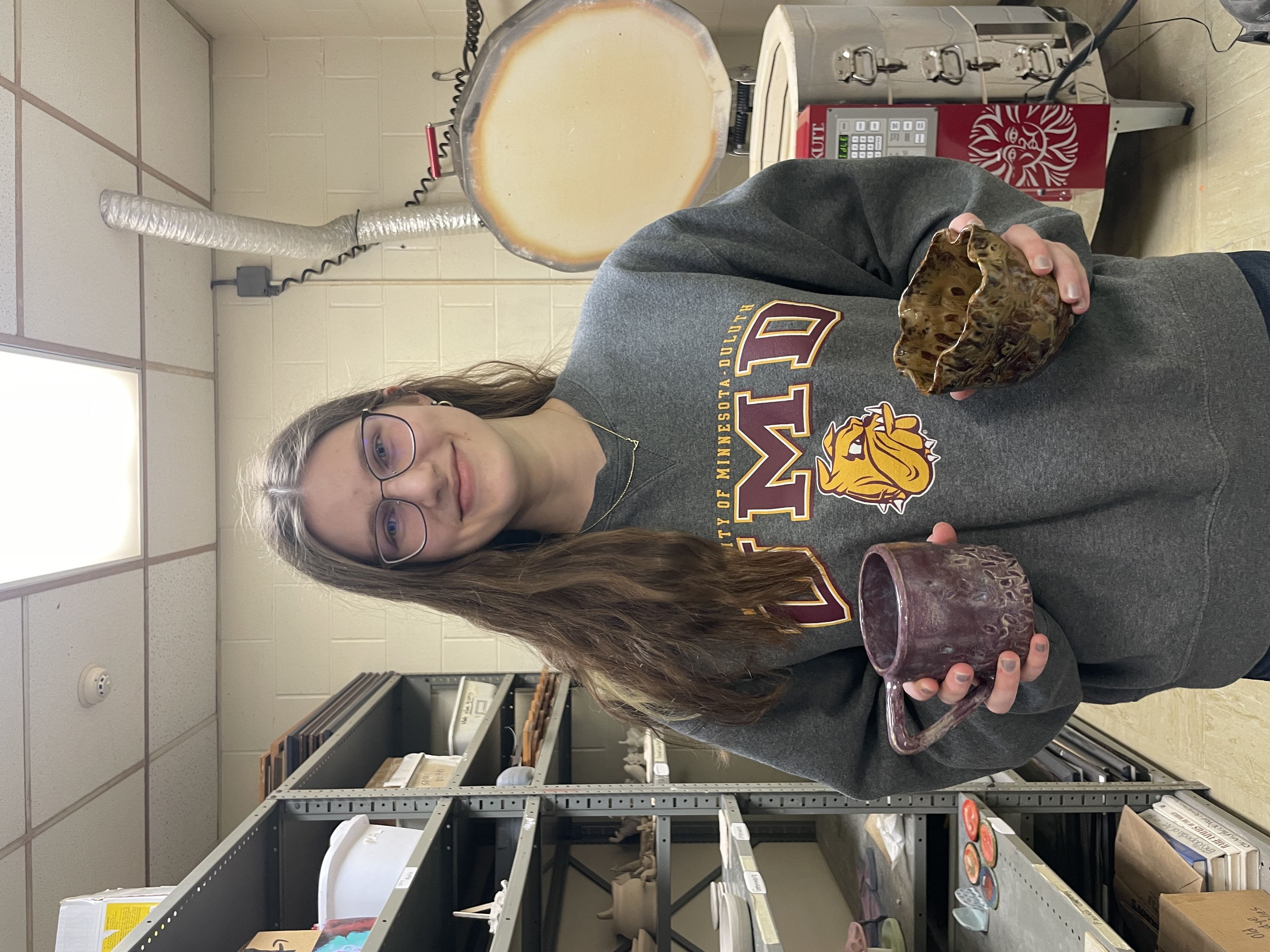 A young woman holds a ceramic bowl and mug, smiling at the camera.