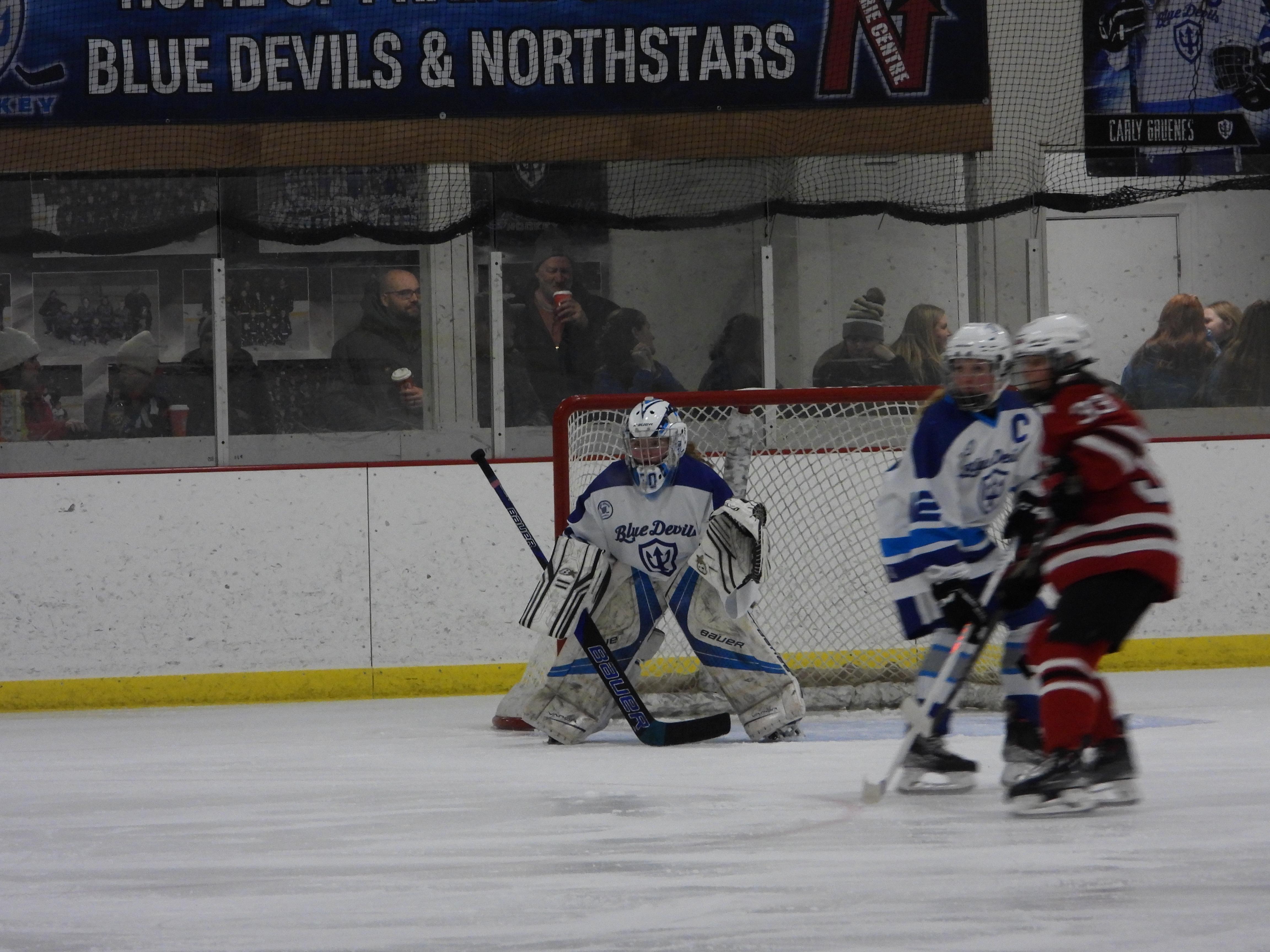 A hockey goalie in blue and white gear prepares for a shot on the ice.