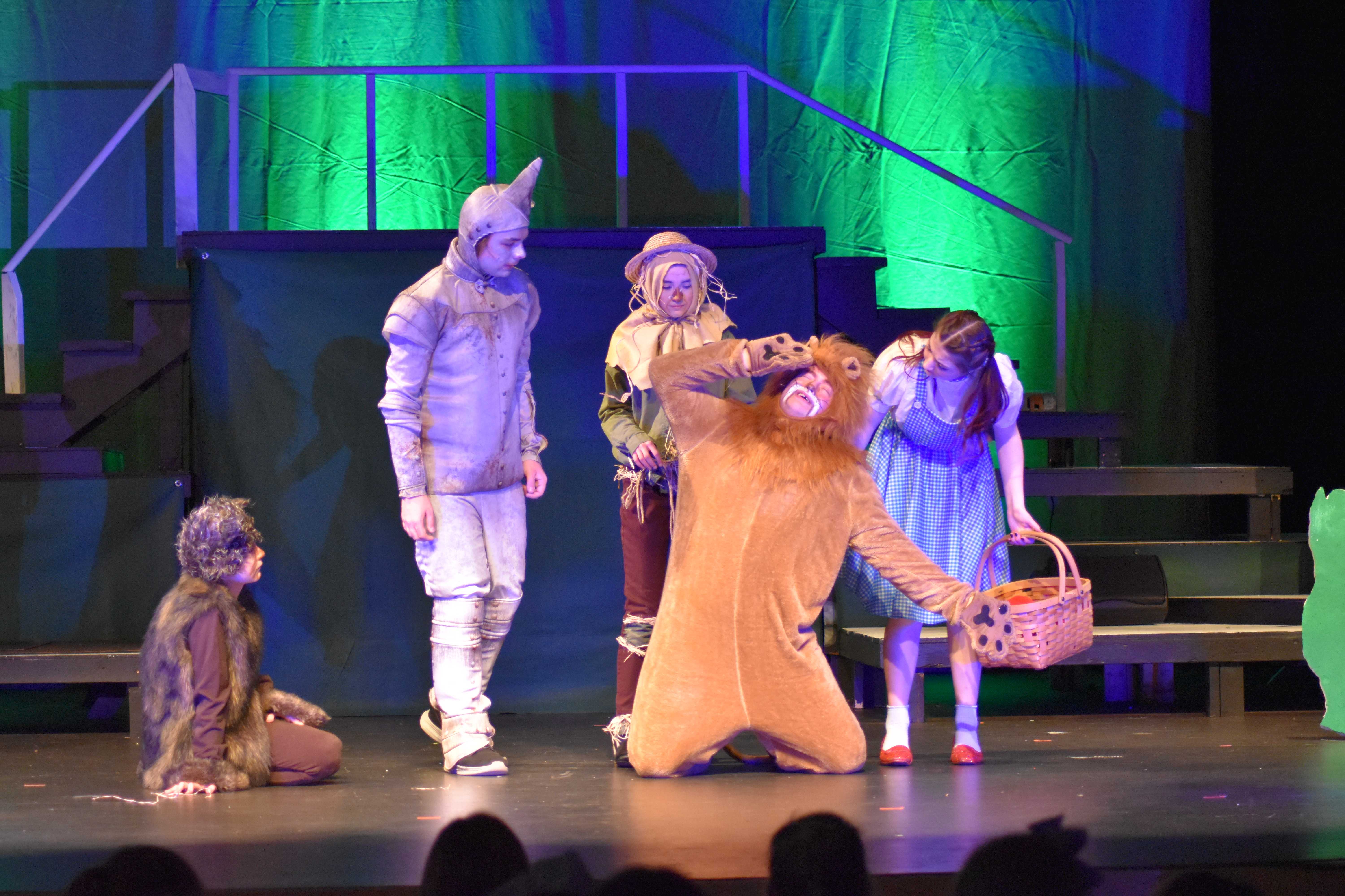 Actors in costumes from The Wizard of Oz perform on a stage.