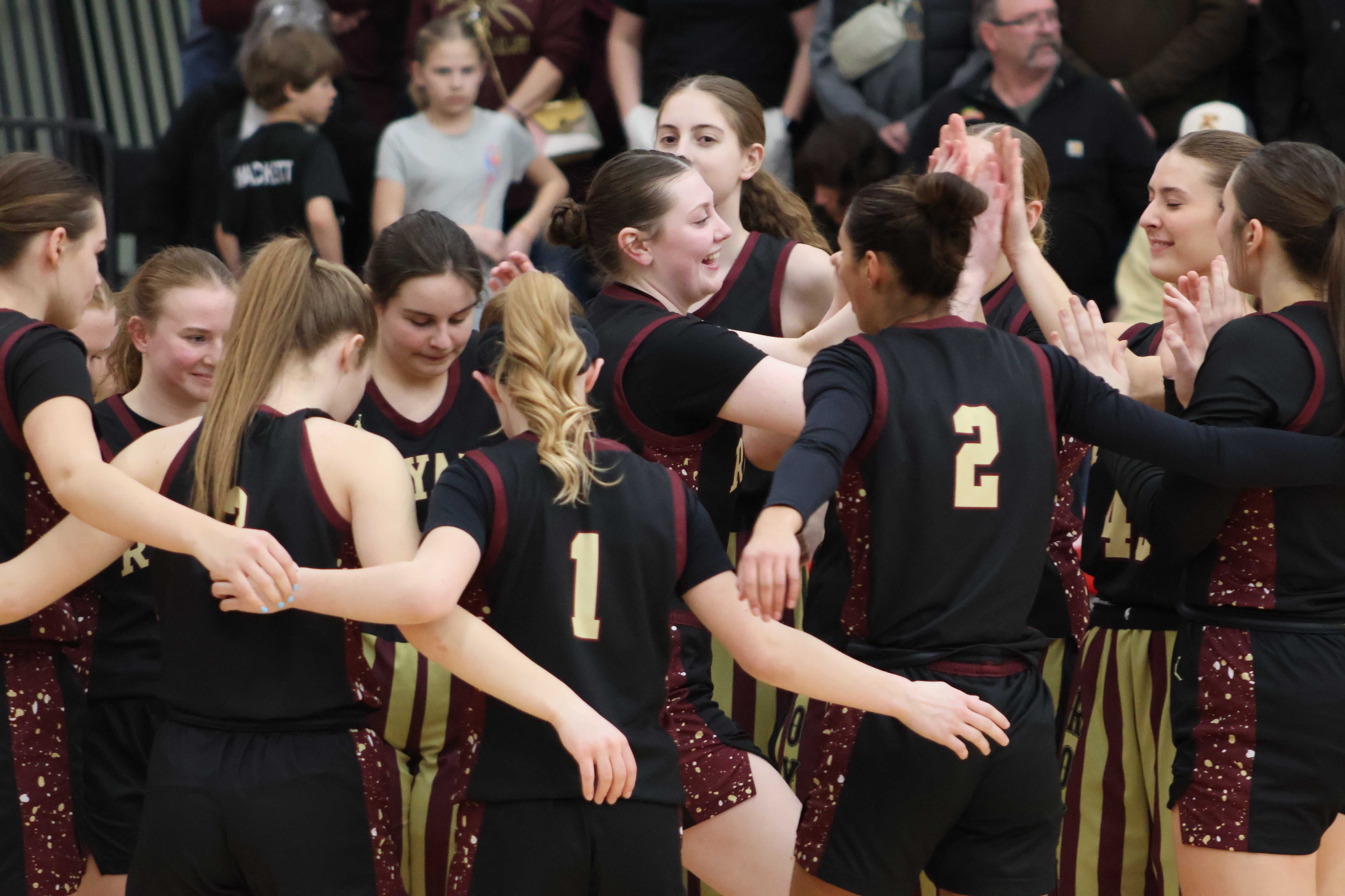 A basketball team huddles together, arms around each other, before a game.