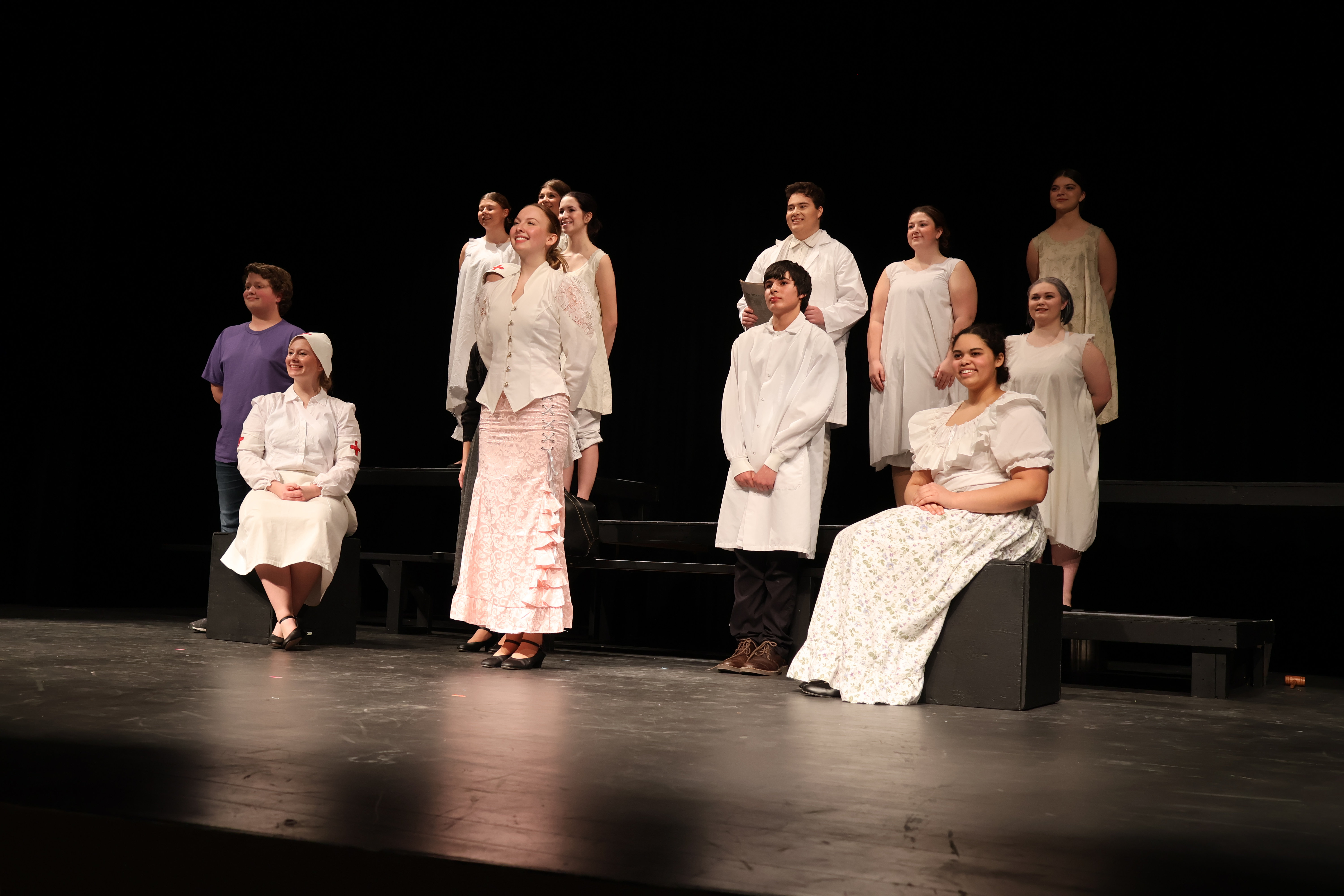 A group of people in white clothing stand on a stage with a dark background.