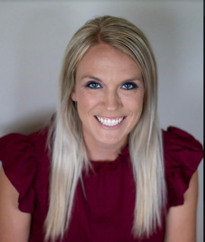 A woman with blonde hair smiles at the camera, wearing a burgundy top.