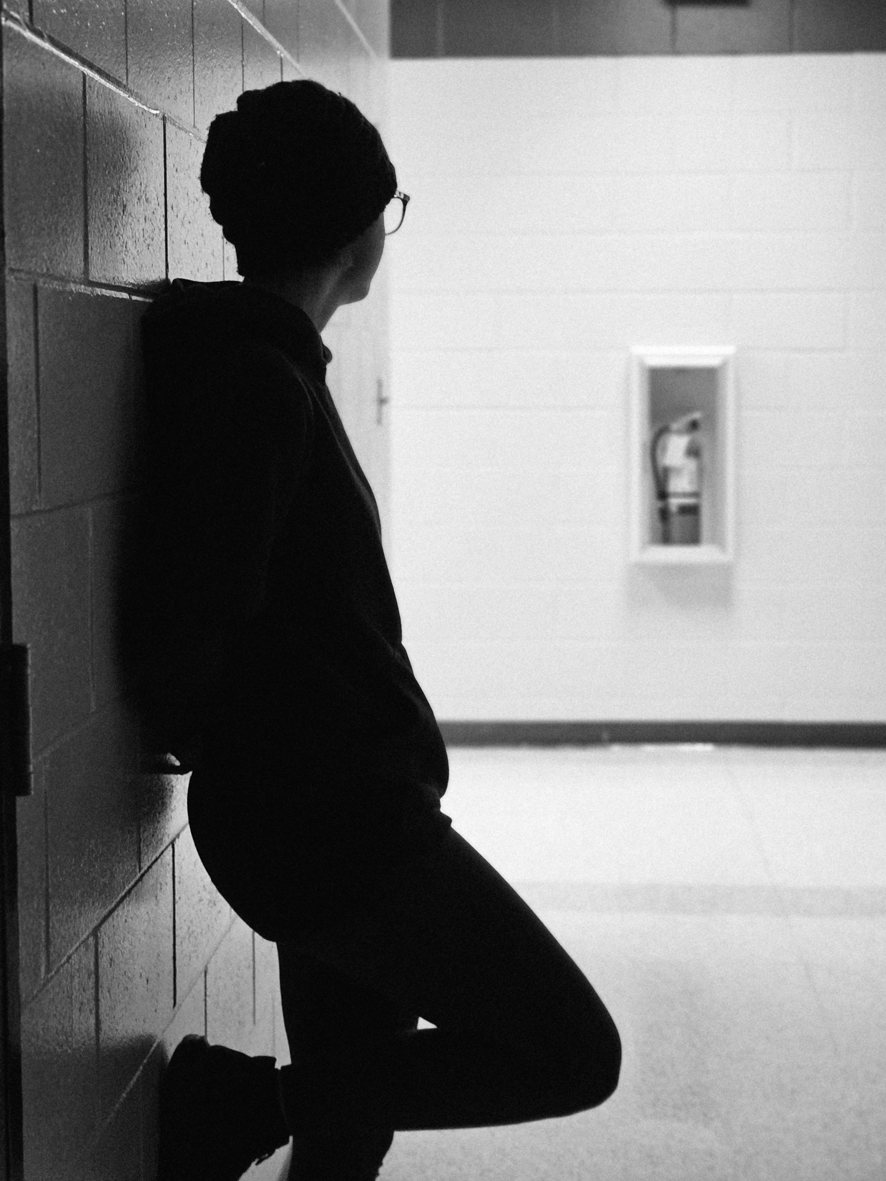 A person in silhouette leans against a wall in a hallway.