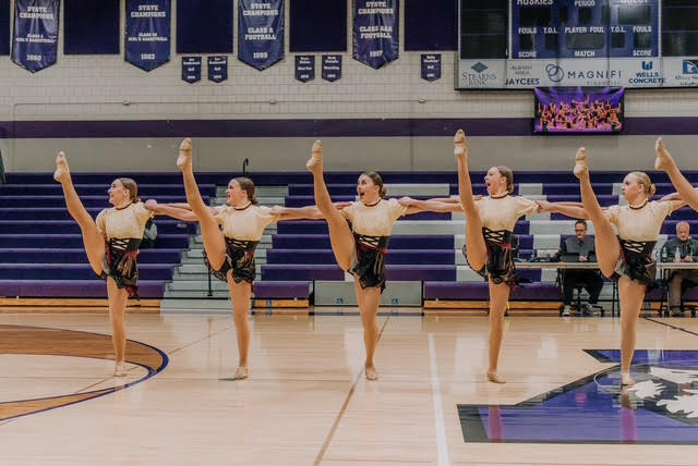 A dance team performs a high kick routine on a basketball court.