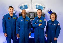 Four astronauts in blue flight suits pose inside a spacecraft.