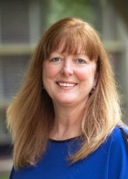 A smiling woman with shoulder-length auburn hair and a blue top.