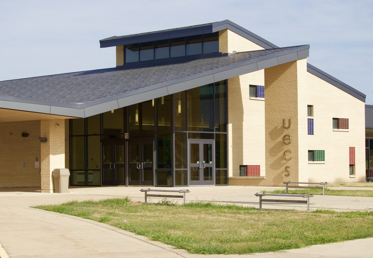 Exterior view of a modern building with a beige brick facade and a dark, angled roof.