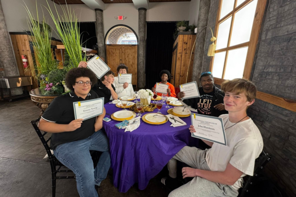 A group of young people sit around a table holding certificates, celebrating an achievement.