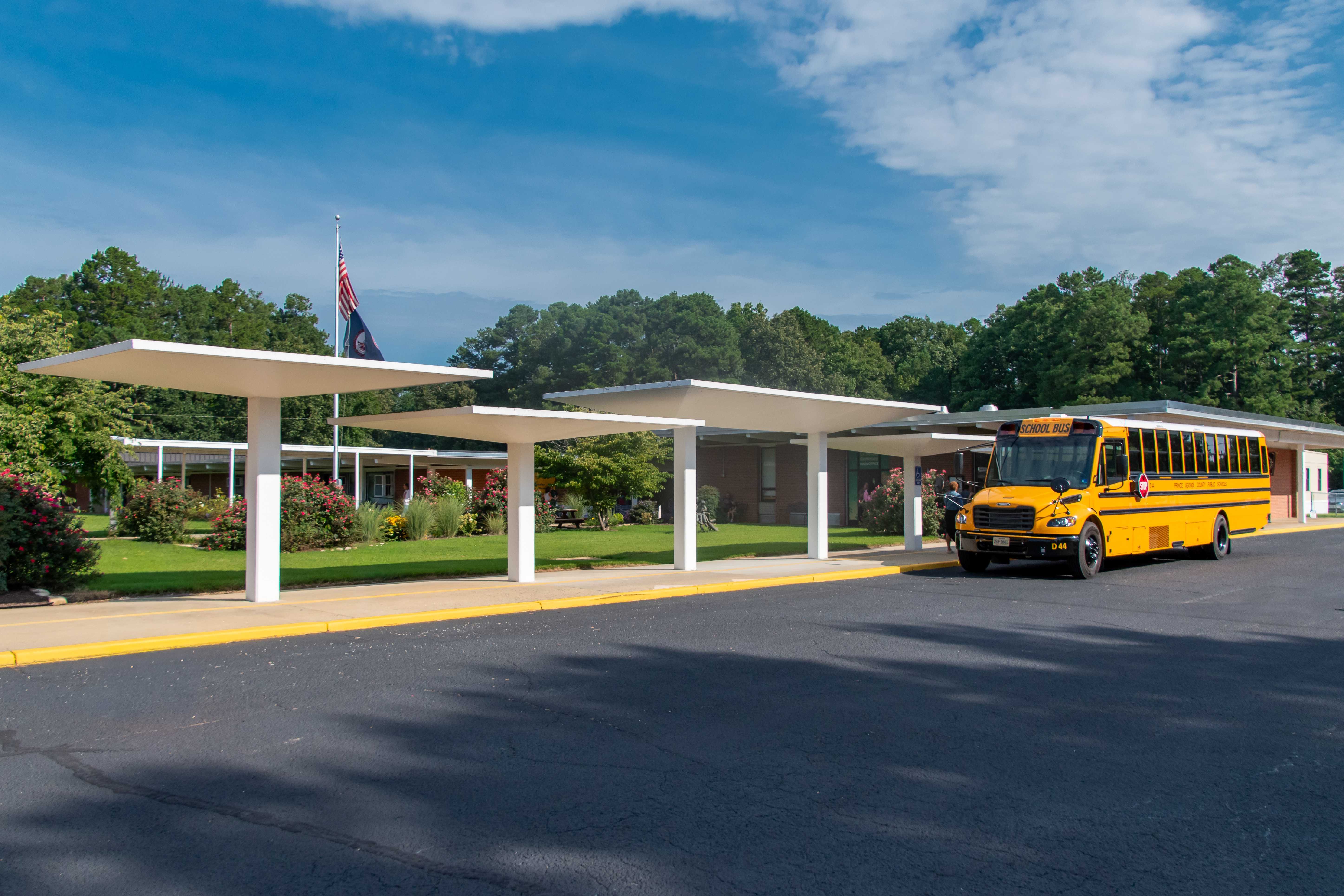 A yellow school bus is parked at a covered bus stop outside Beazley Elementary.
