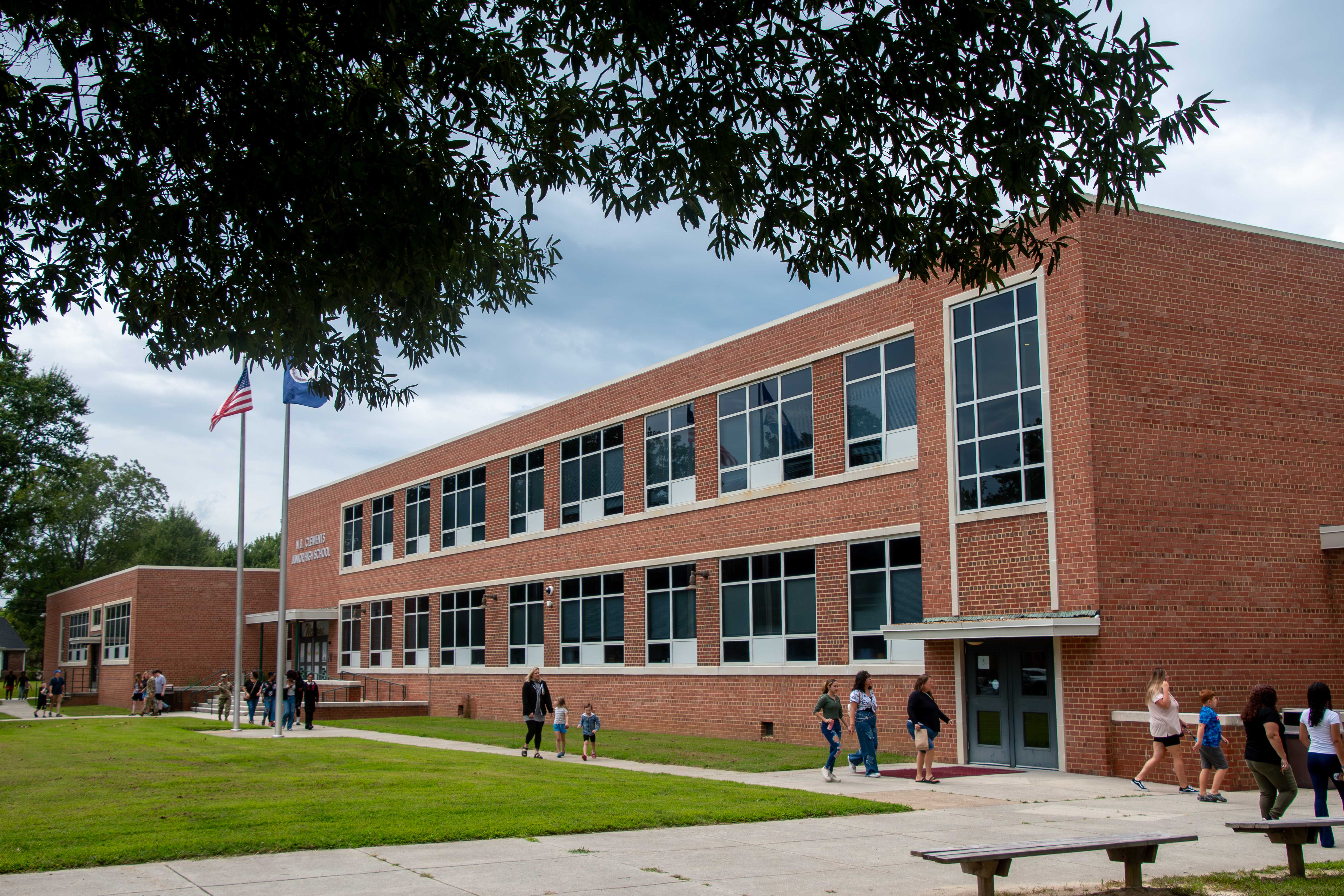 A brick school building with large windows and students walking outside.