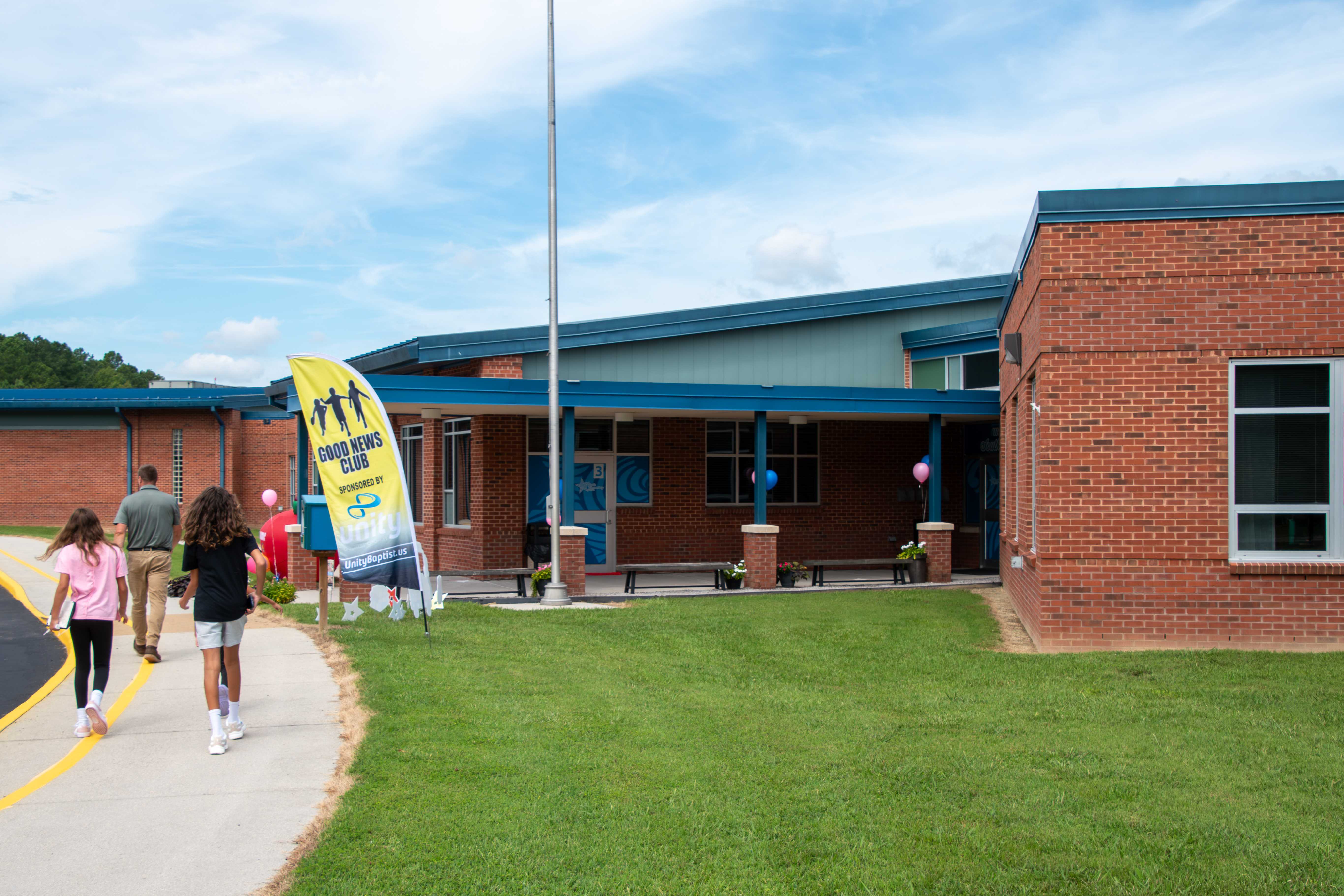 Children walk towards a brick school building with a blue roof.