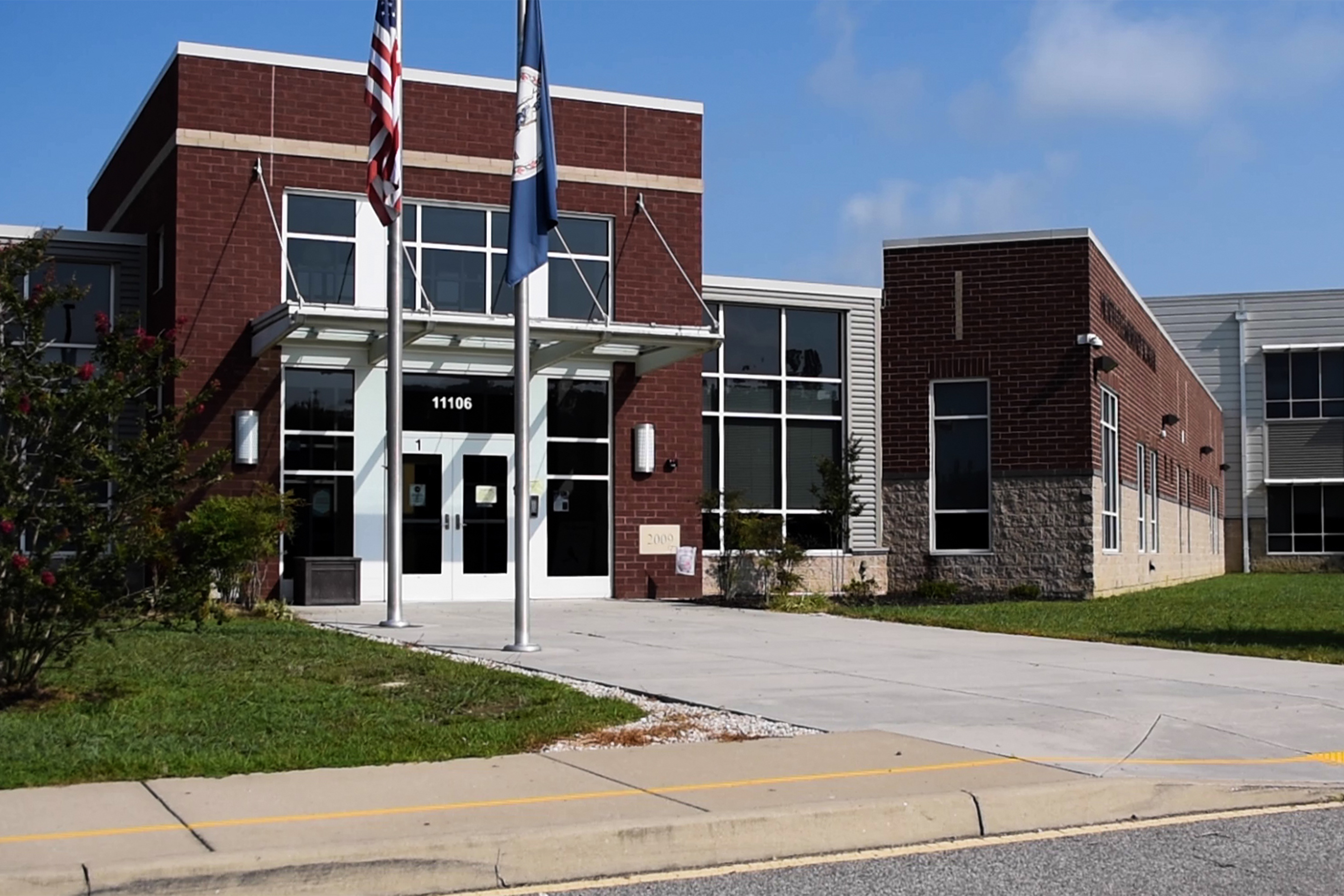 The brick facade of a modern school building with large windows and flags.