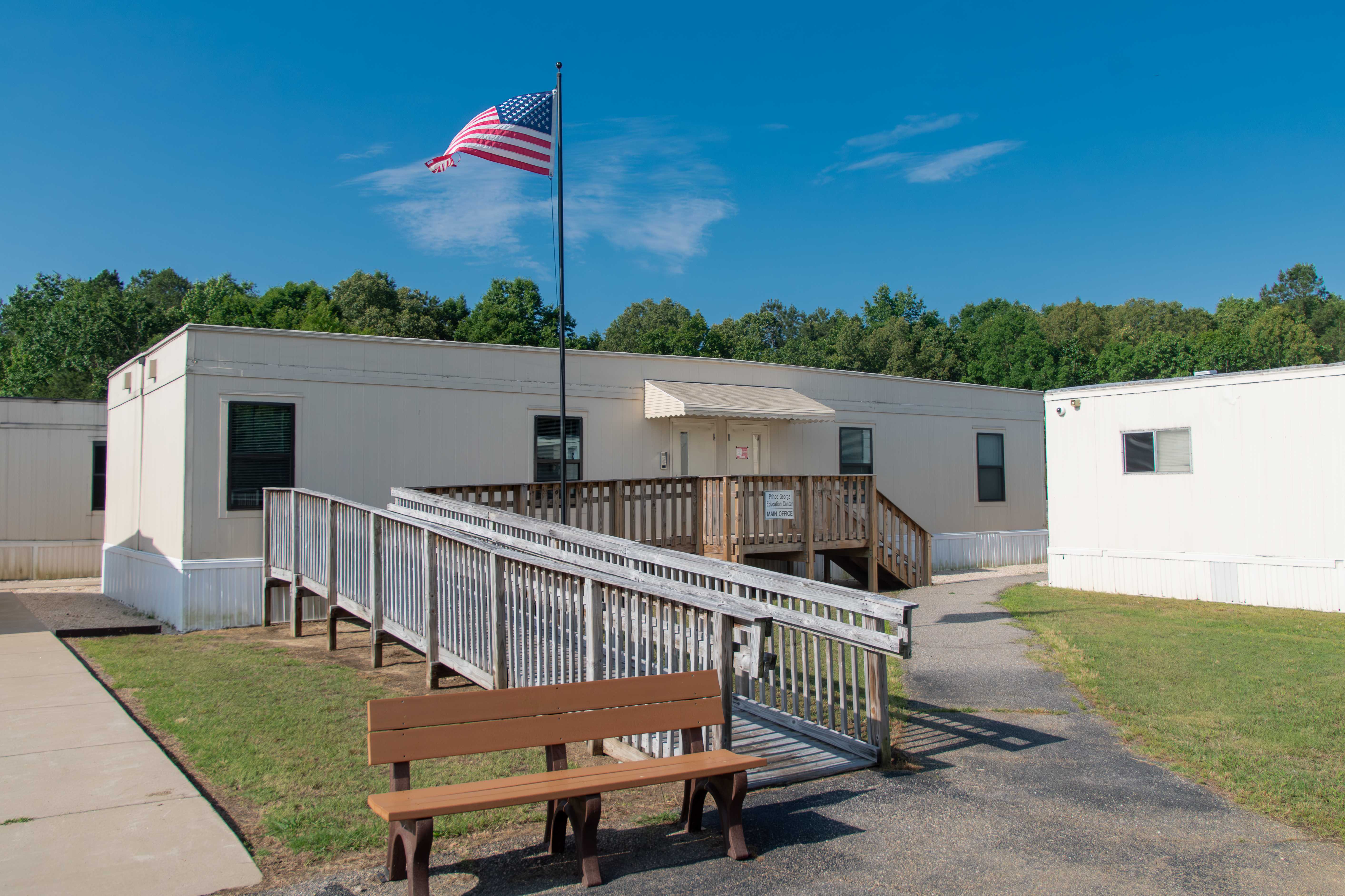 A single-story building with a ramp and stairs leading to the entrance, under a blue sky.
