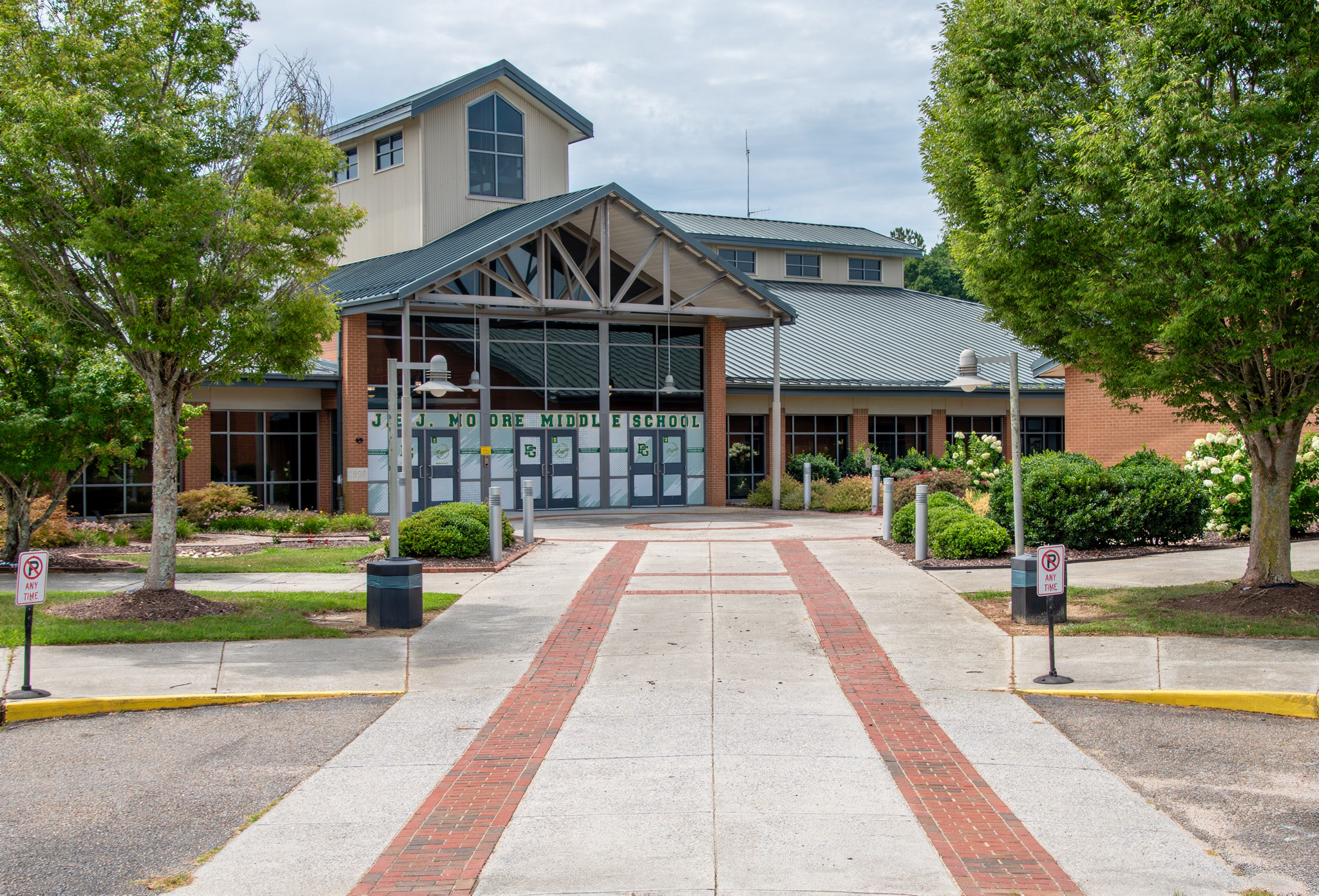 A modern building with large glass doors and windows, surrounded by trees and a paved walkway.