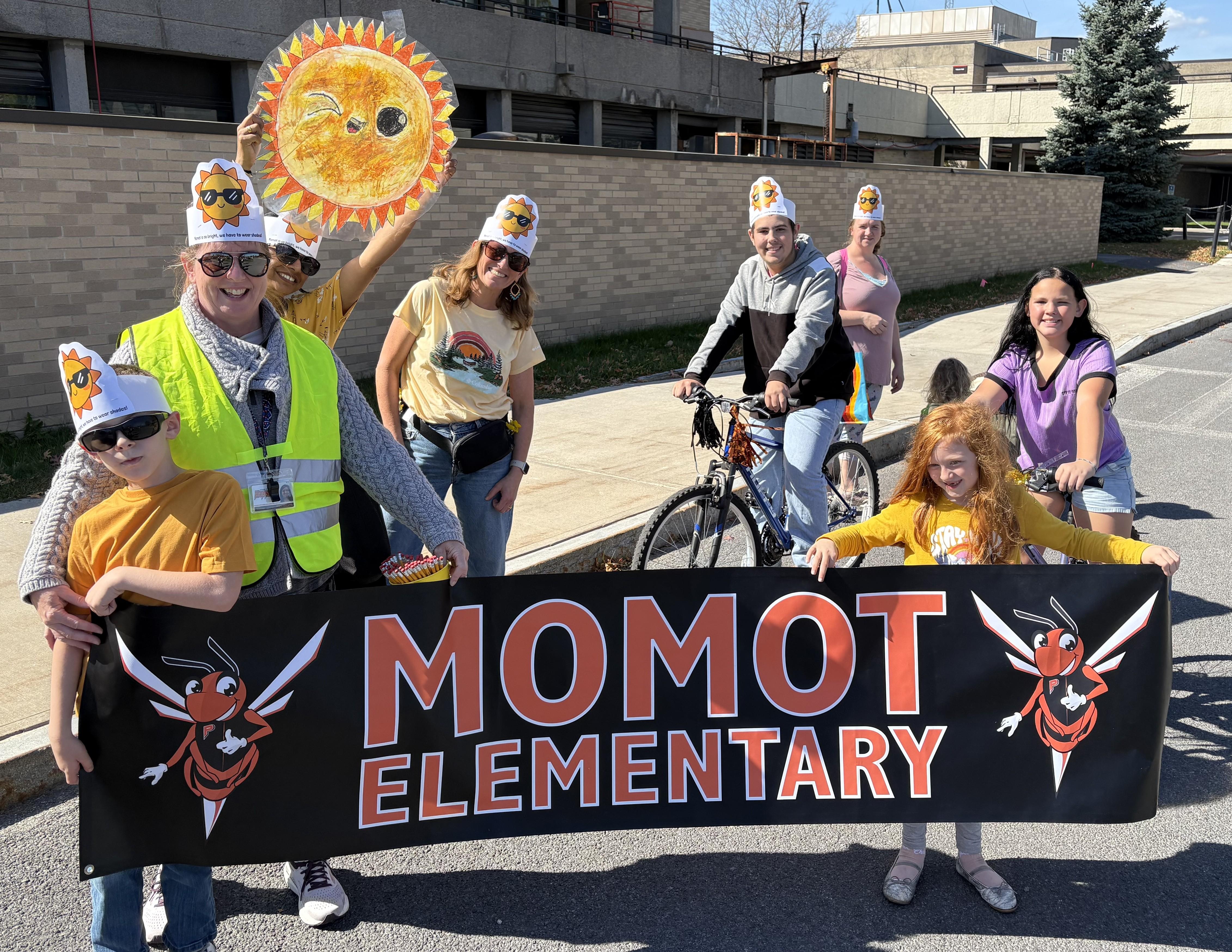 A group of people in costumes hold a banner that reads 'MOMOT ELEMENTARY'.
