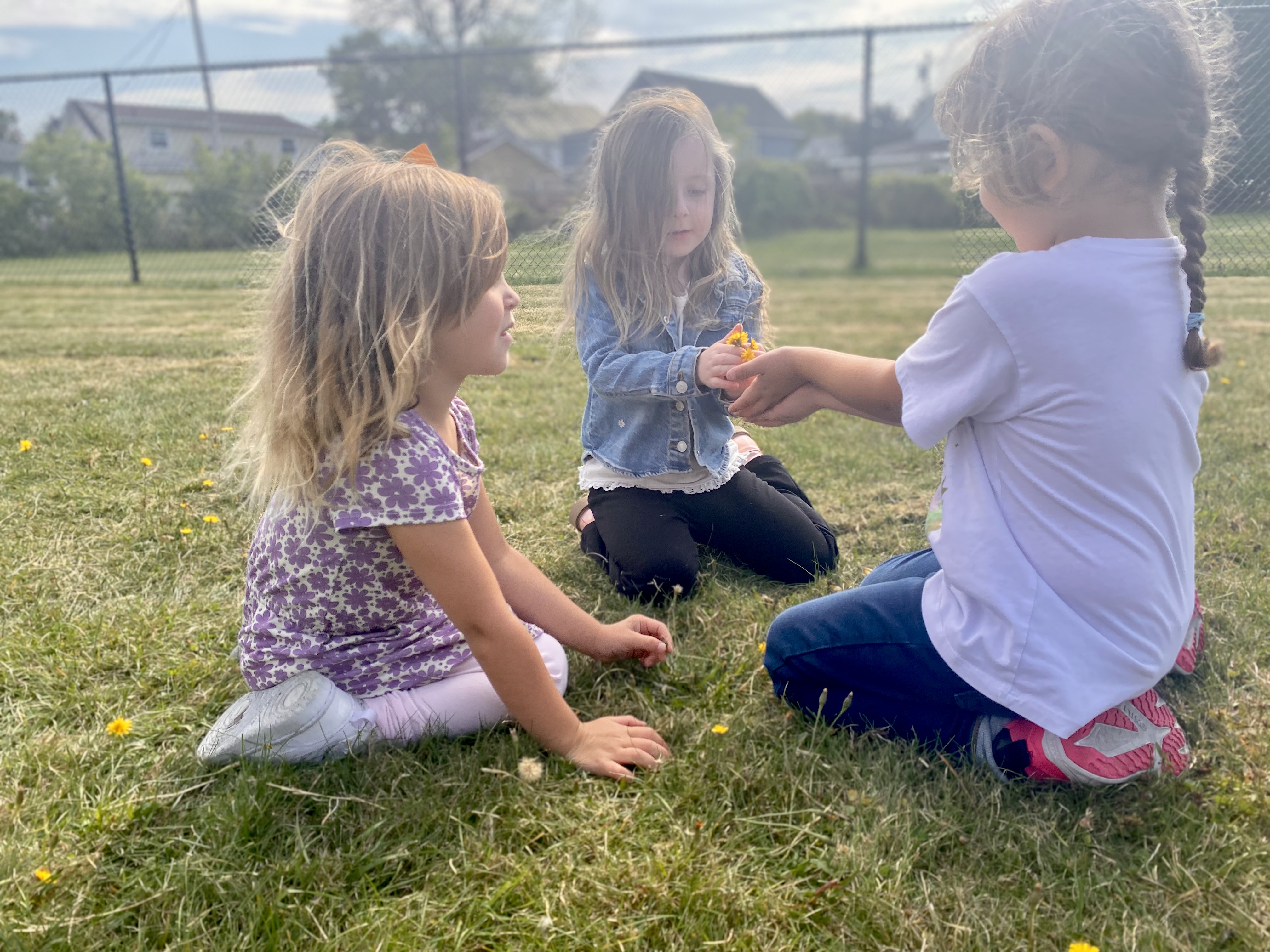 Three young girls sit on a grassy field, engaged in a game.