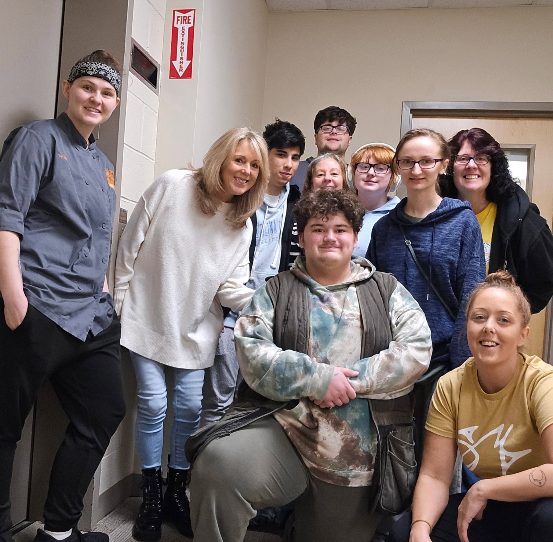 A diverse group of students and an adult pose for a photo in a hallway.