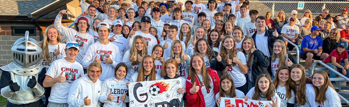 A large group of people, mostly young women, pose for a photo in bleachers, many wearing white shirts.