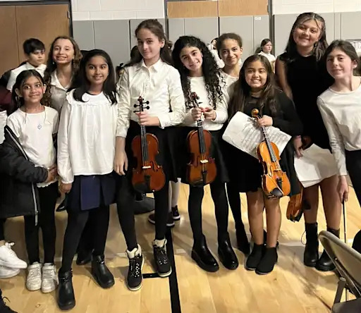 A group of young violinists and their instructor pose for a photo after a performance.
