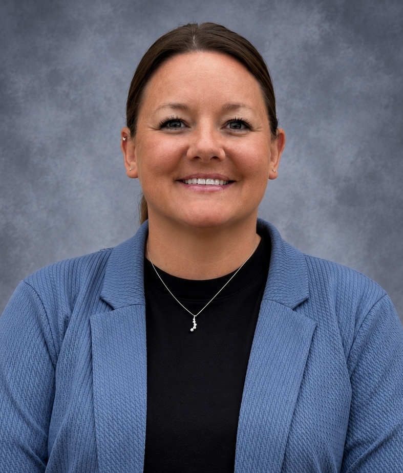 A woman with brown hair pulled back smiles at the camera, wearing a blue blazer over a black shirt.