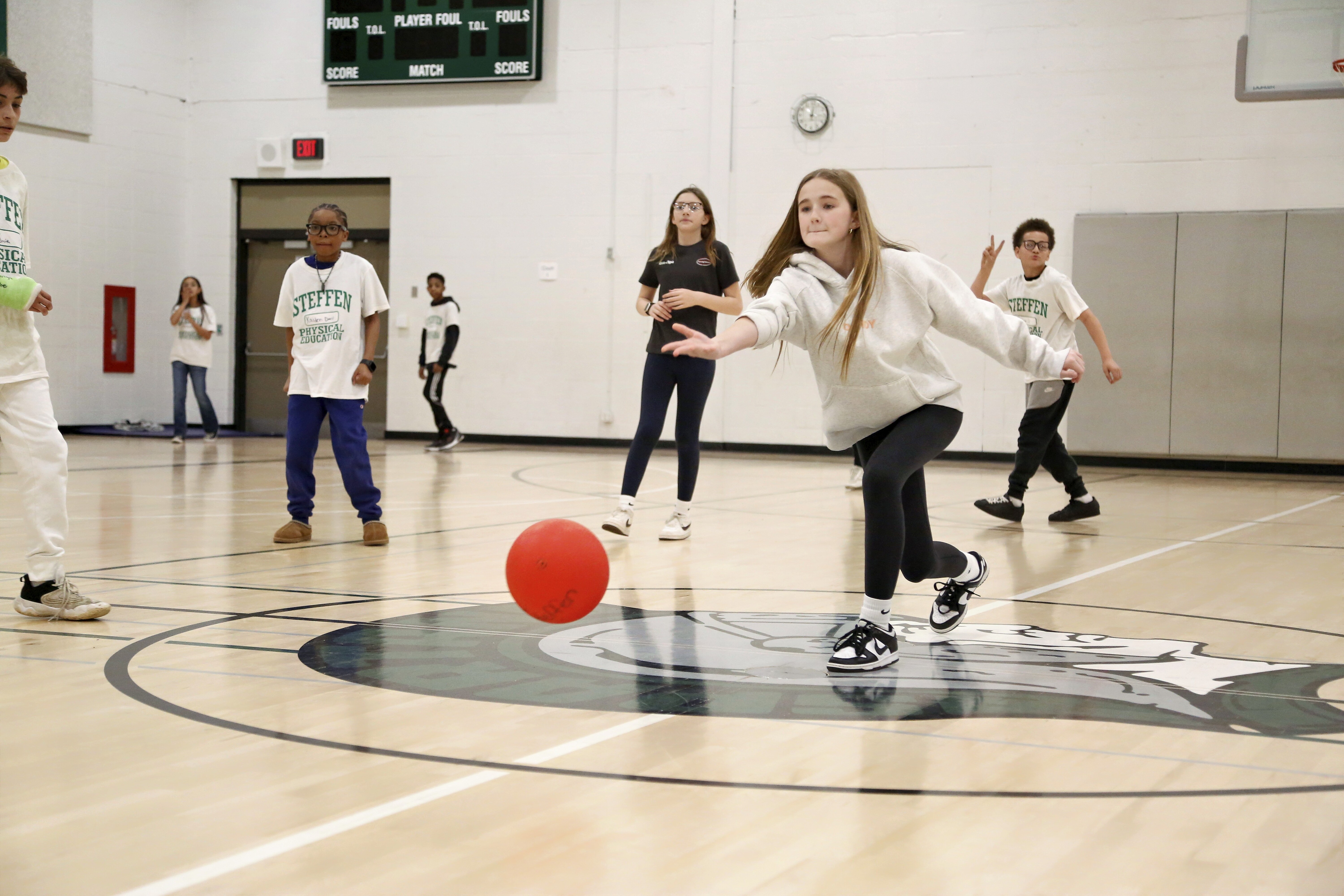 A group of students plays a game of dodgeball in a school gymnasium.