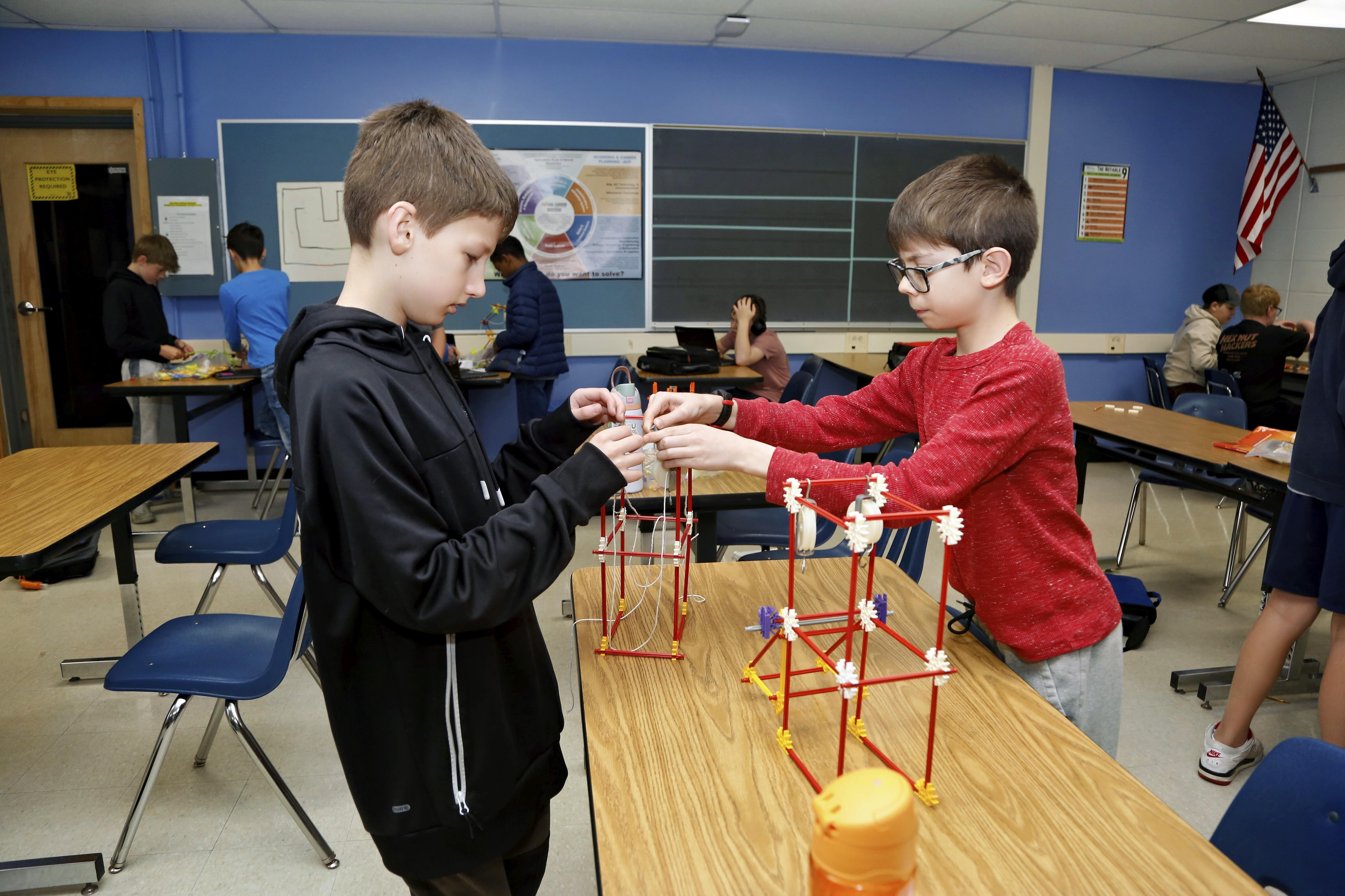 Two boys collaborate on a STEM project, building with straws and connectors at a classroom table.