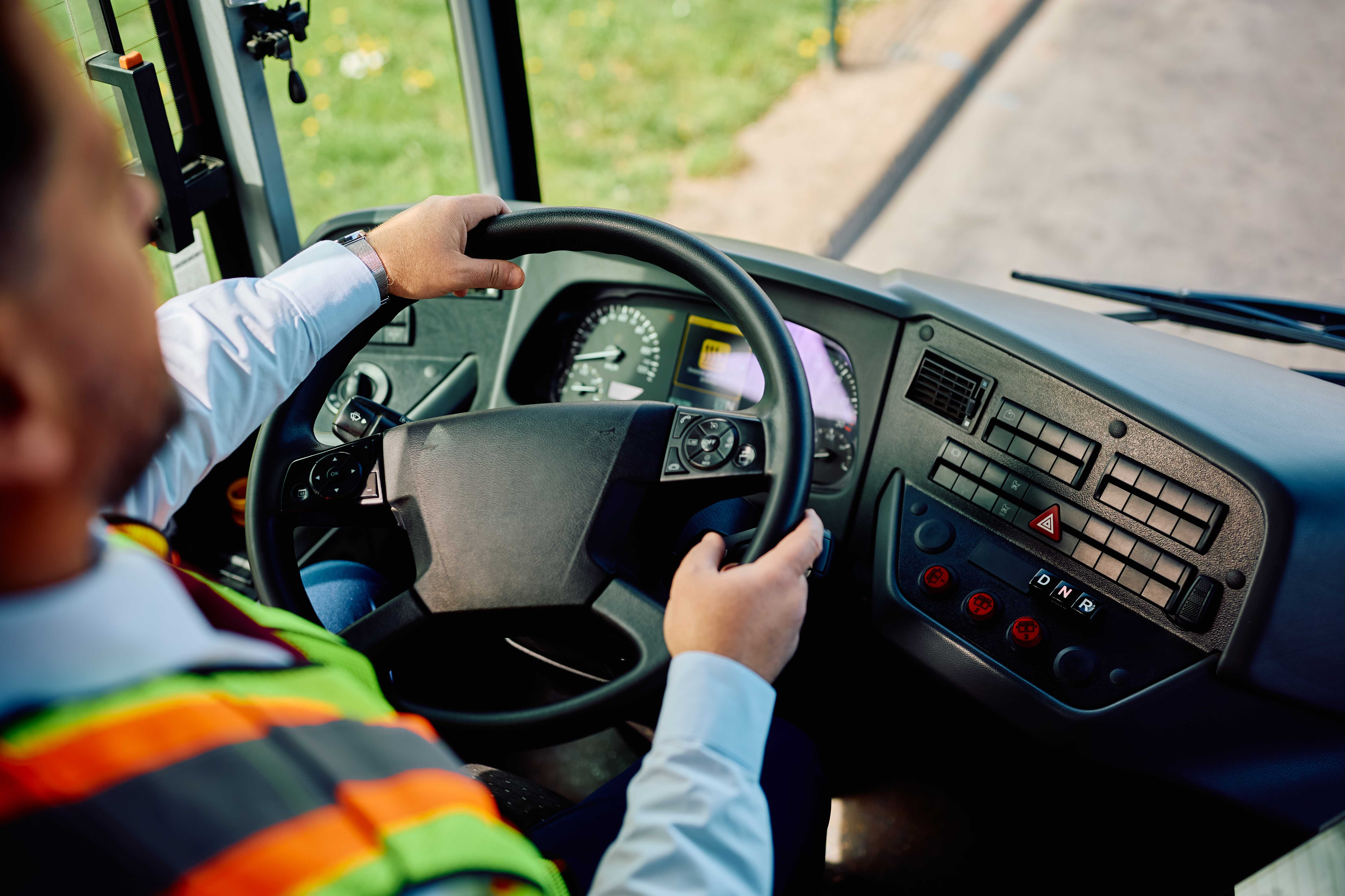A person wearing a high-visibility vest drives a large vehicle, hands on the steering wheel.