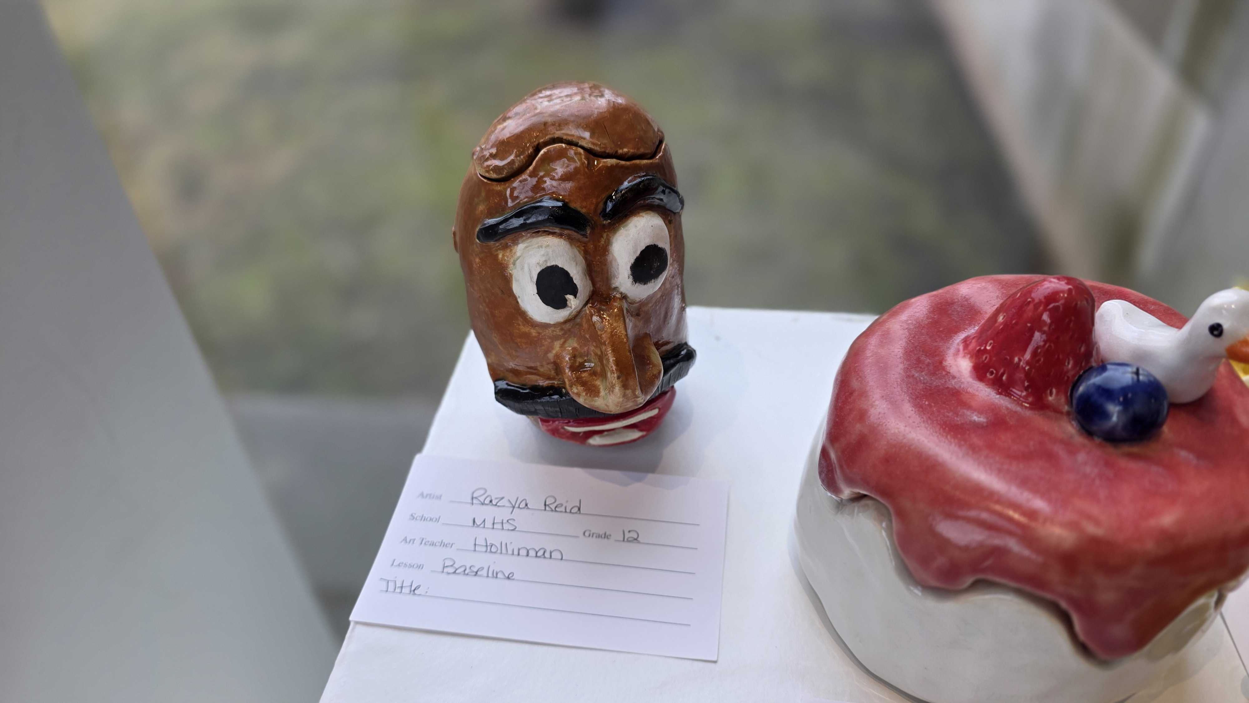 A whimsical, carved wooden owl figure with wide eyes sits next to a decorative ceramic cake.