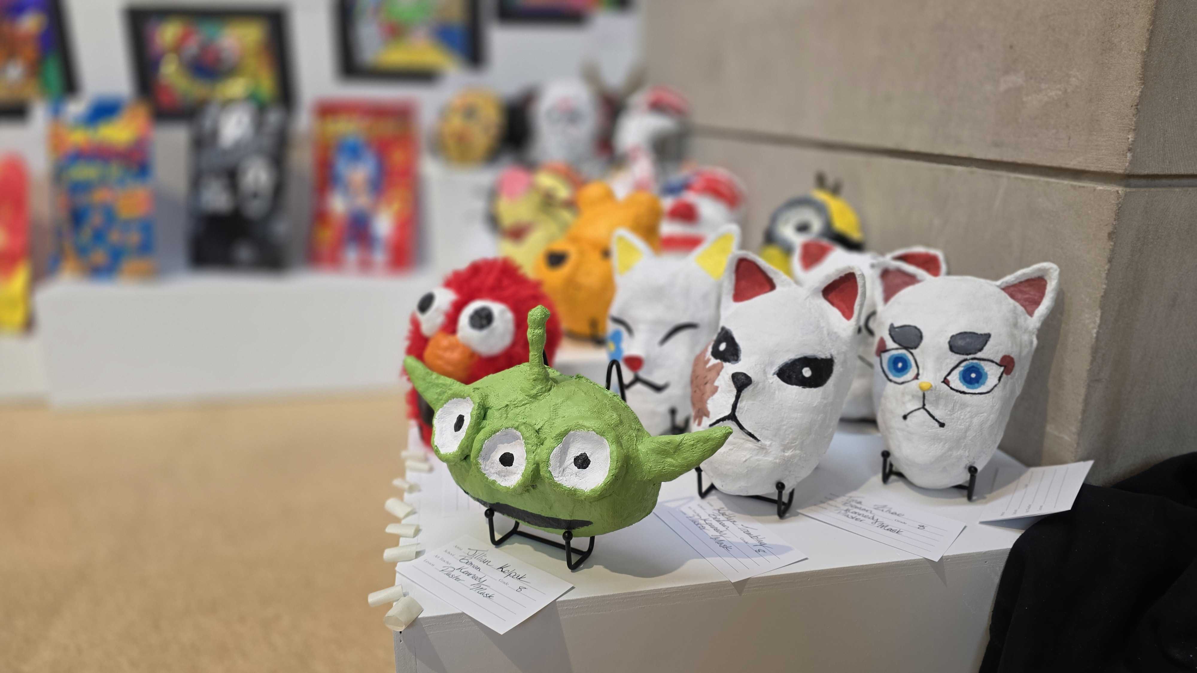 A collection of colorful, whimsical ceramic figures displayed on a white cloth.