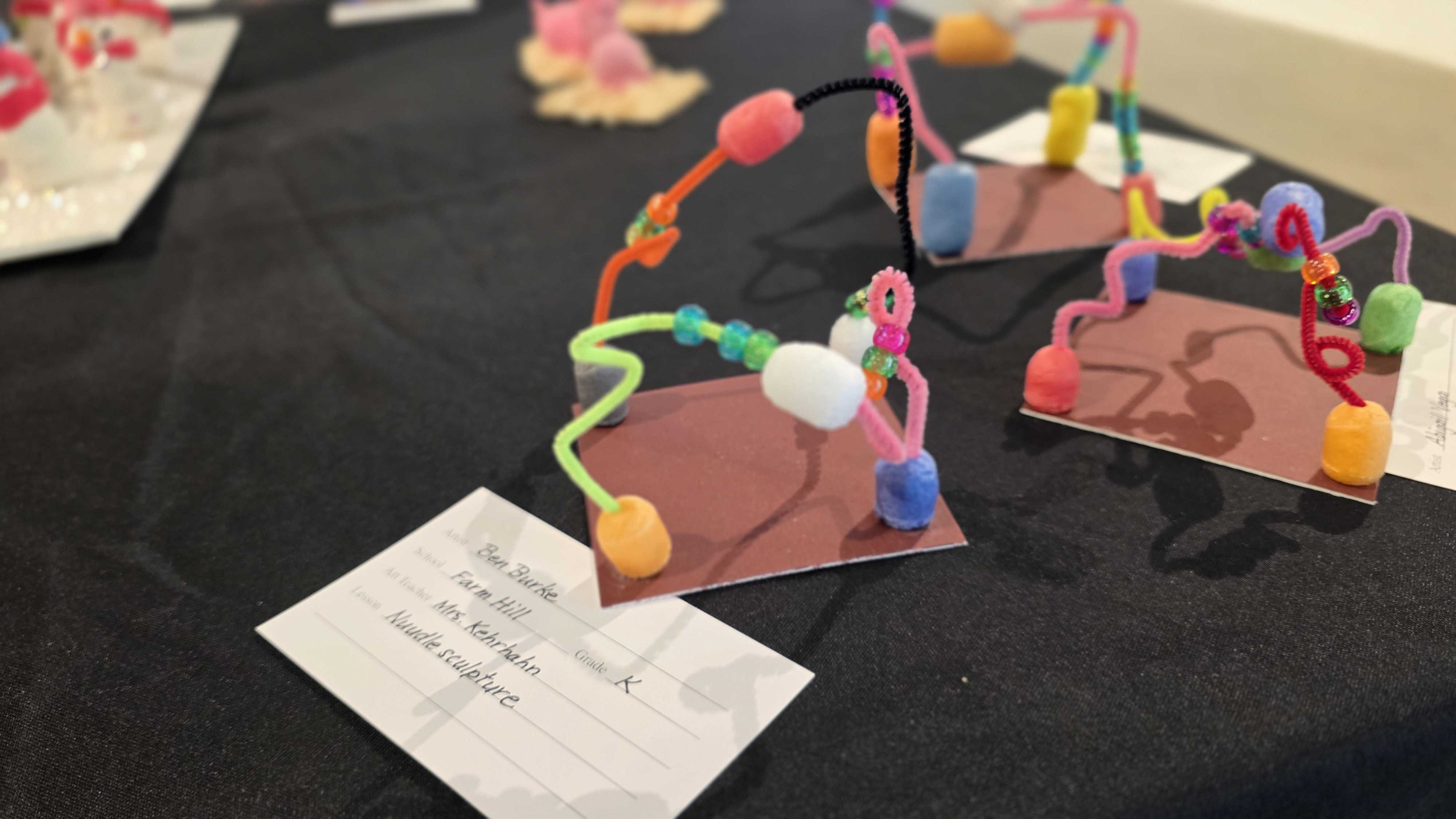 Colorful, handmade crafts with pipe cleaners and beads displayed on a dark surface.