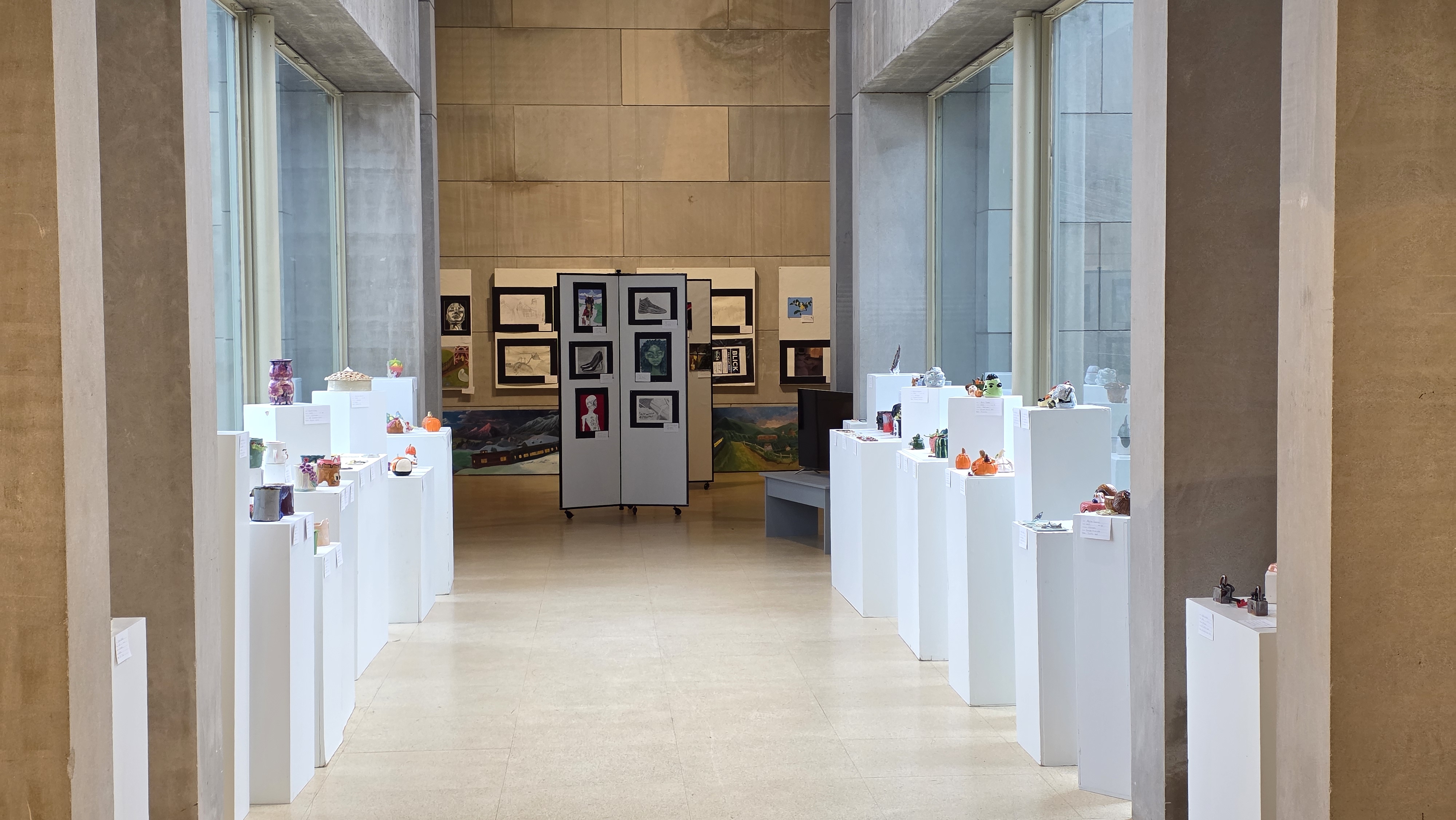 An art gallery hallway with framed artwork displayed on walls and pedestals.