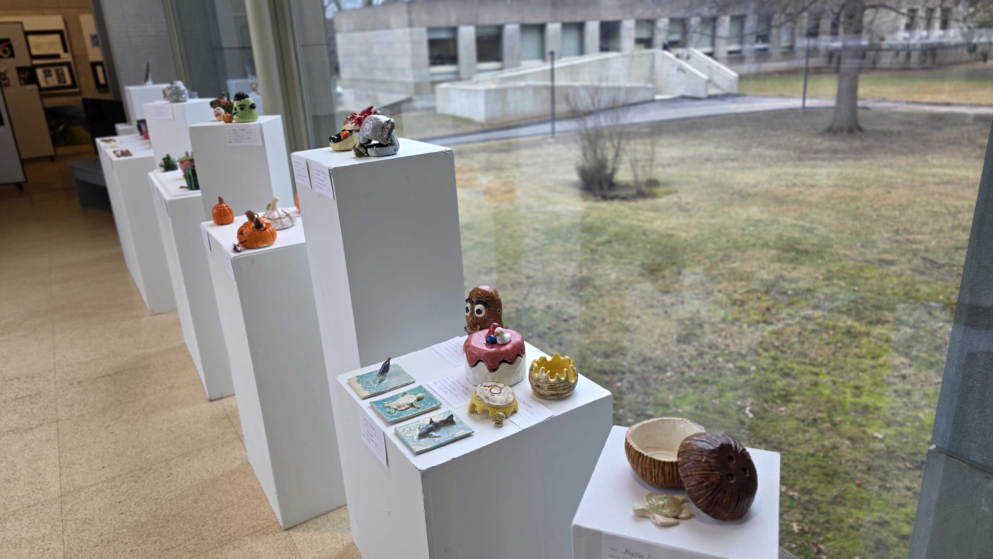 Art exhibition featuring various sculptures and crafts displayed on white pedestals.