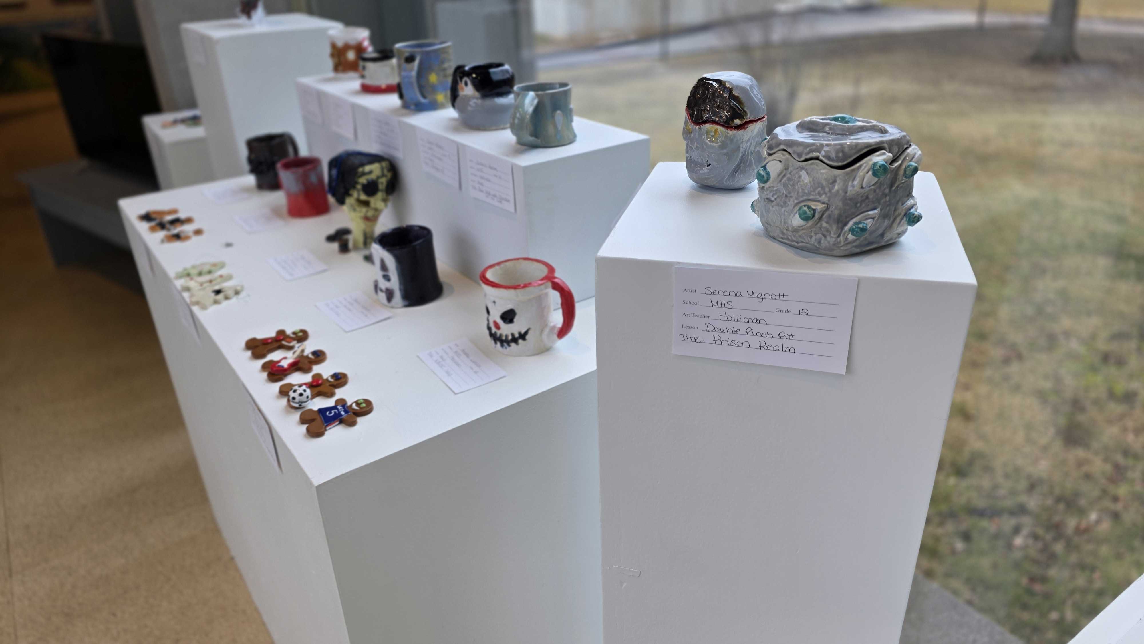 A display of various watches and small accessories arranged on white pedestals.