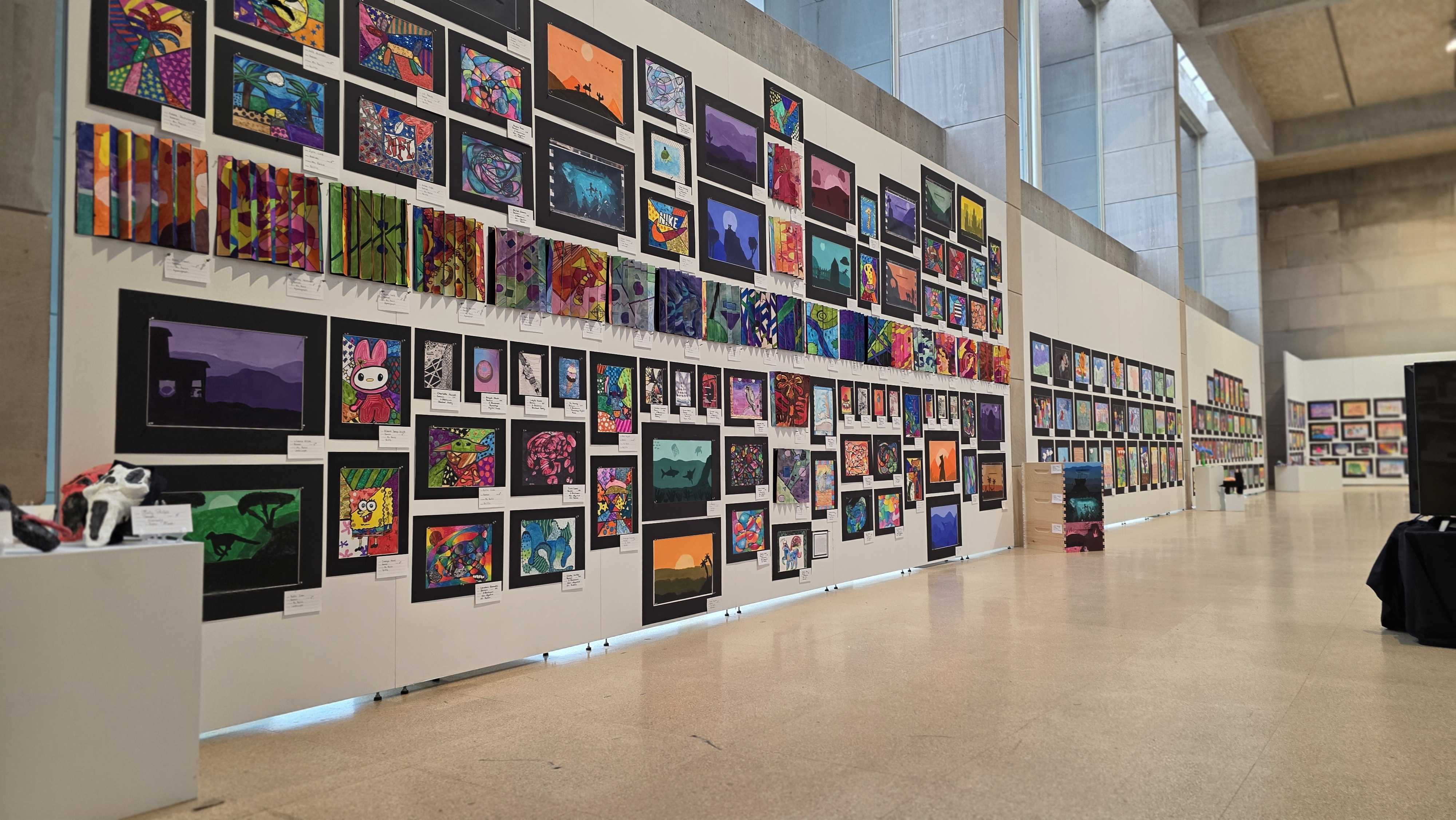 A wide shot of a gallery wall displaying a large collection of colorful digital art on screens.