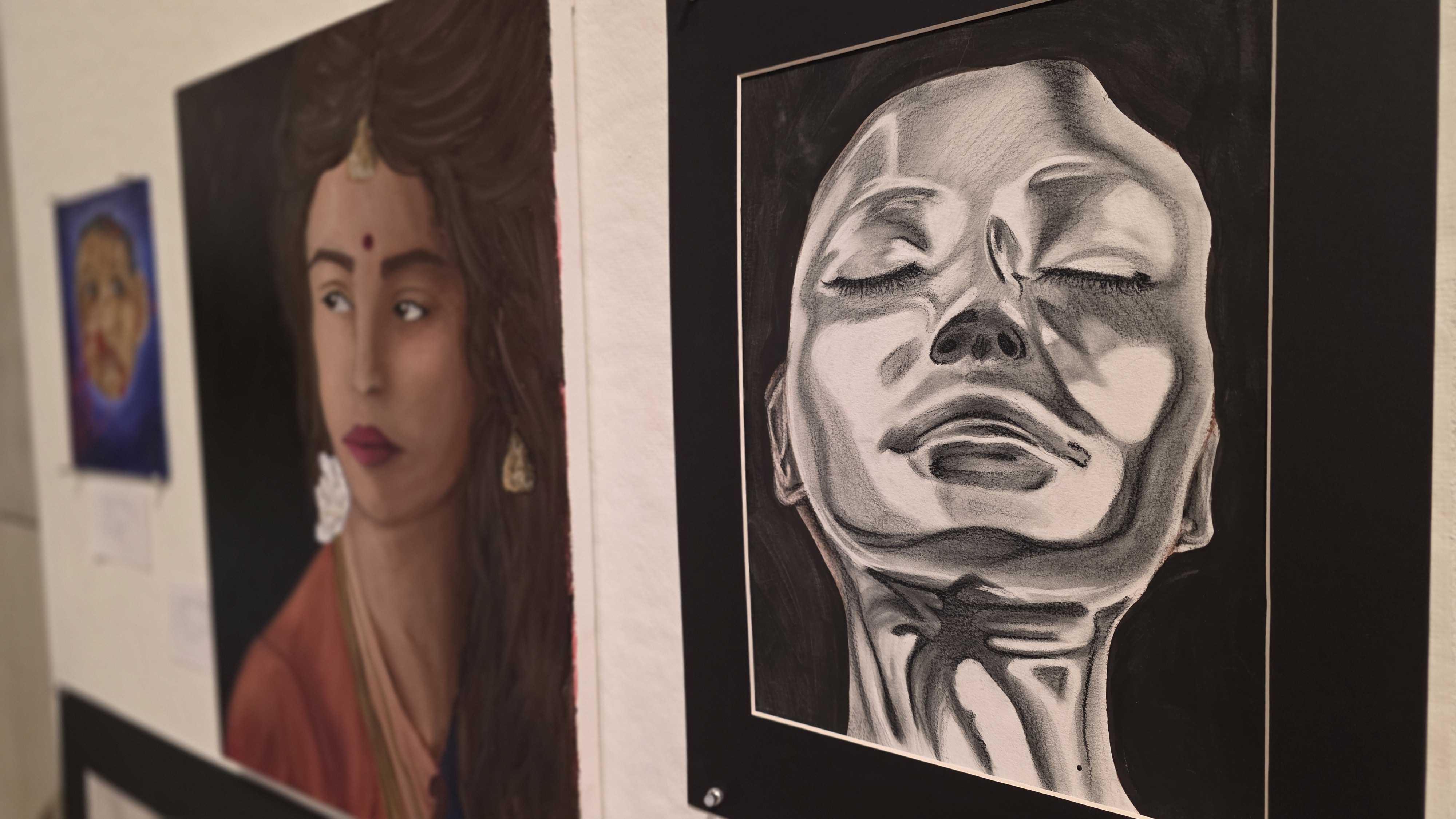 Two framed artworks are displayed on a white wall: a portrait of a woman and a grayscale sculpture of a face.