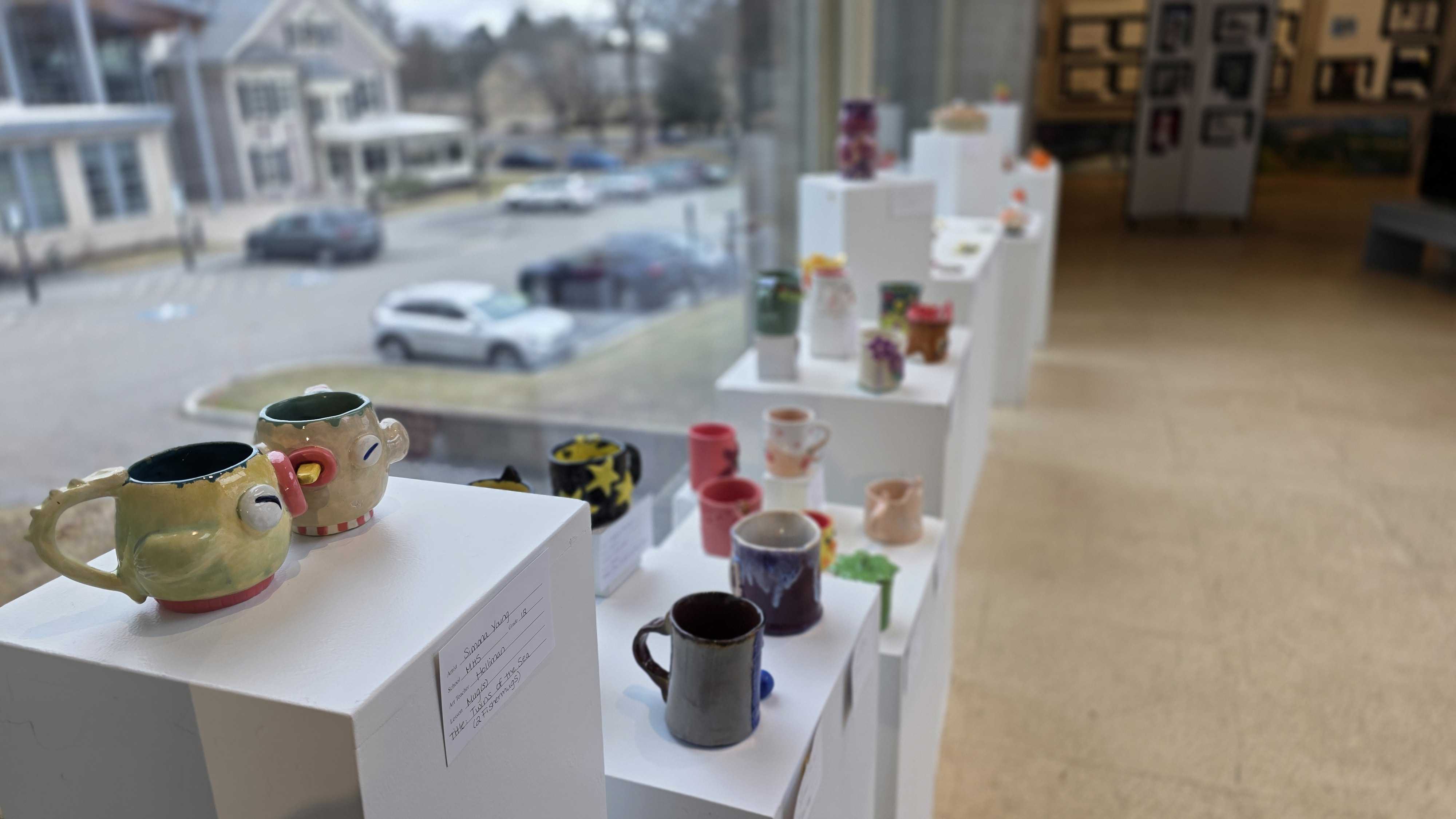 Ceramic mugs and decorative items displayed on white shelves in a shop window.