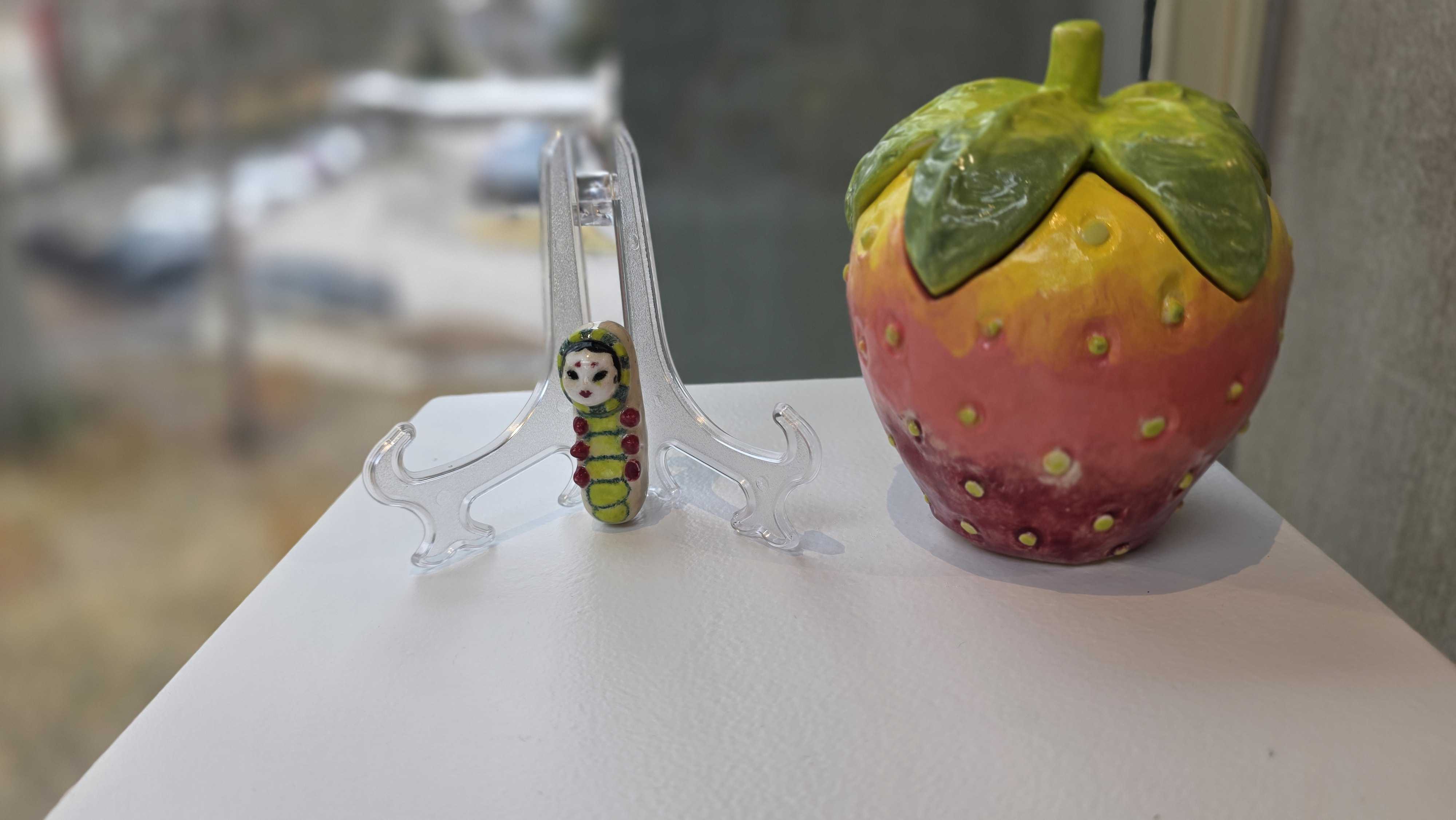 A caterpillar crawls on a clear plastic stand next to a colorful strawberry-shaped decorative object.