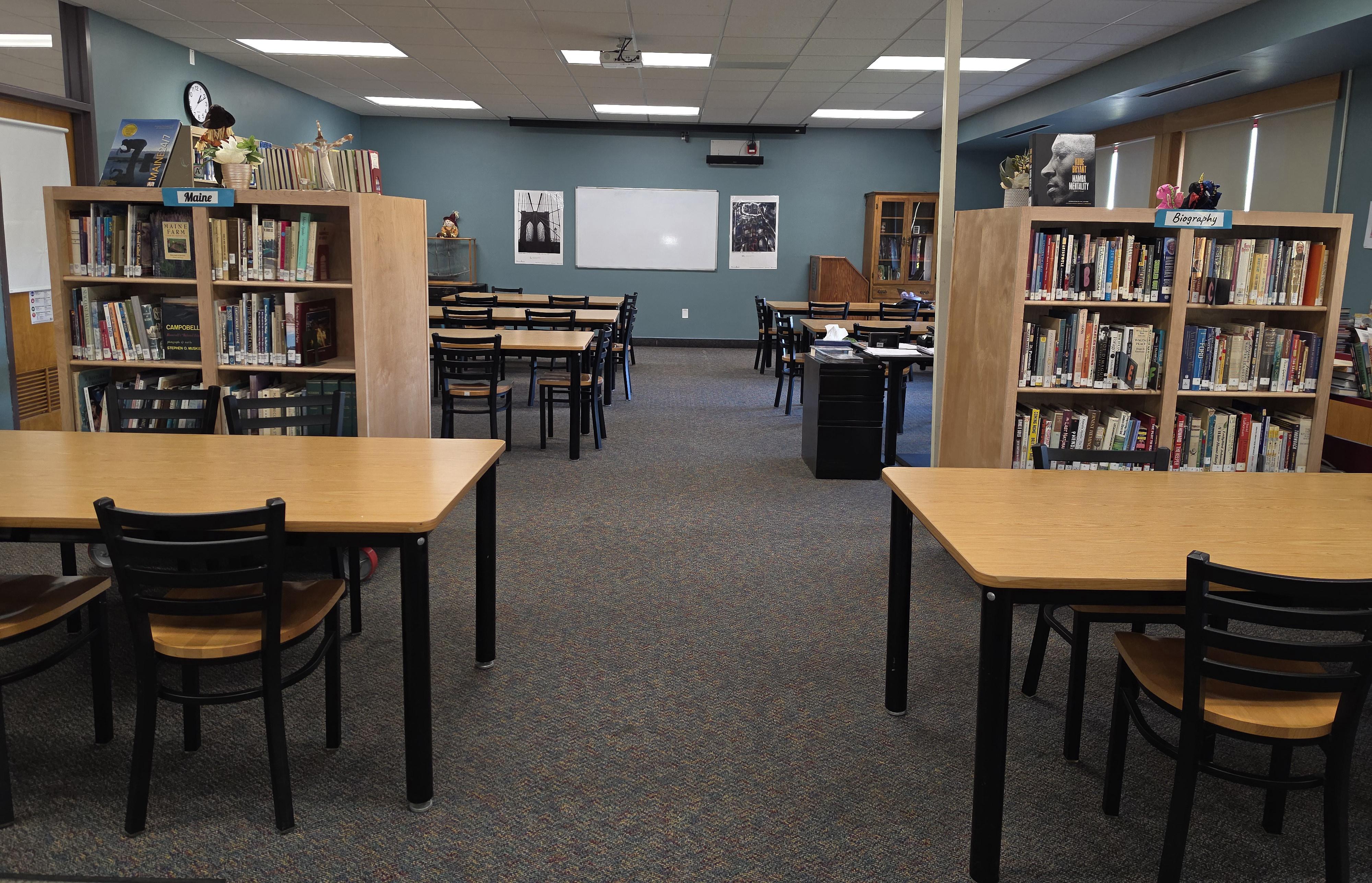 A quiet, brightly lit library featuring wooden tables, chairs, and tall bookshelves.