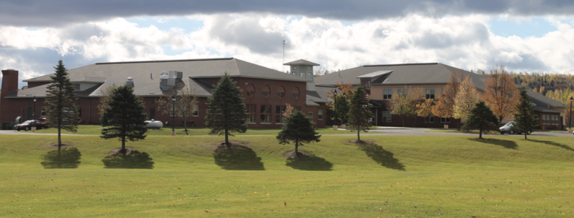 A wide view of a large building complex set behind a green grassy lawn with several small trees.