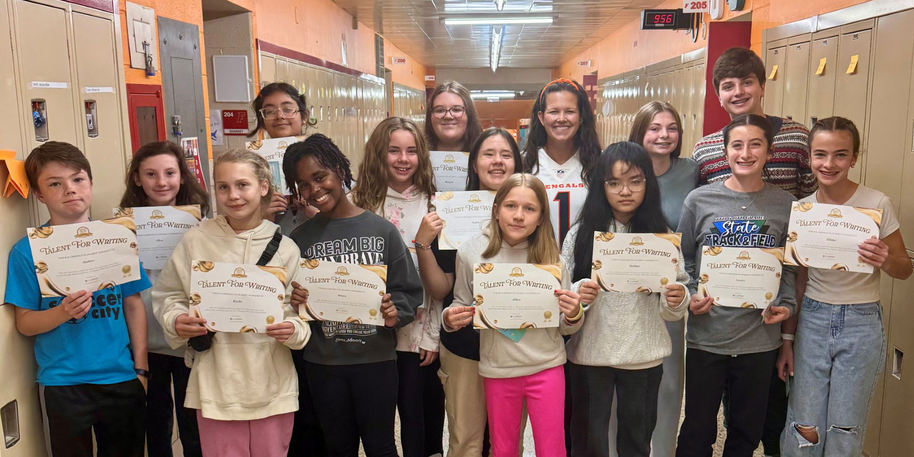 A group of students stand in a school hallway, holding certificates.