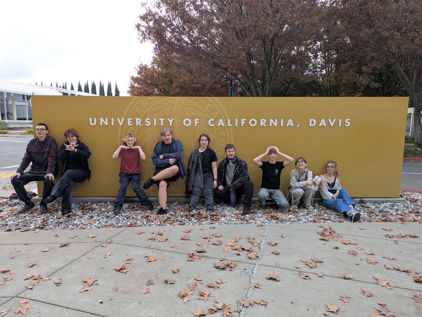 A group of people pose in front of a yellow sign that reads "University of California, Davis" outdoors.