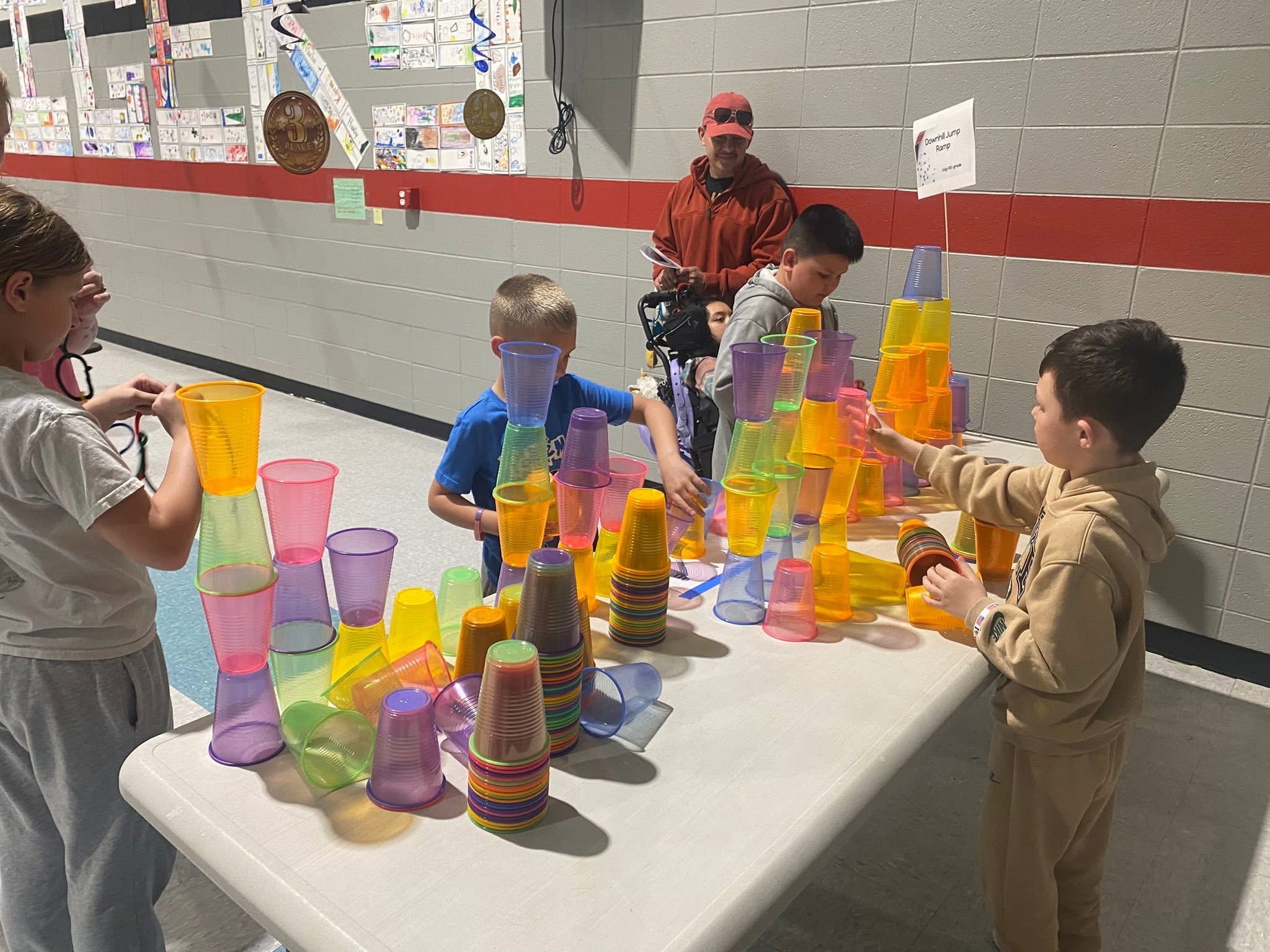 Children build tall towers with colorful plastic cups on a table.