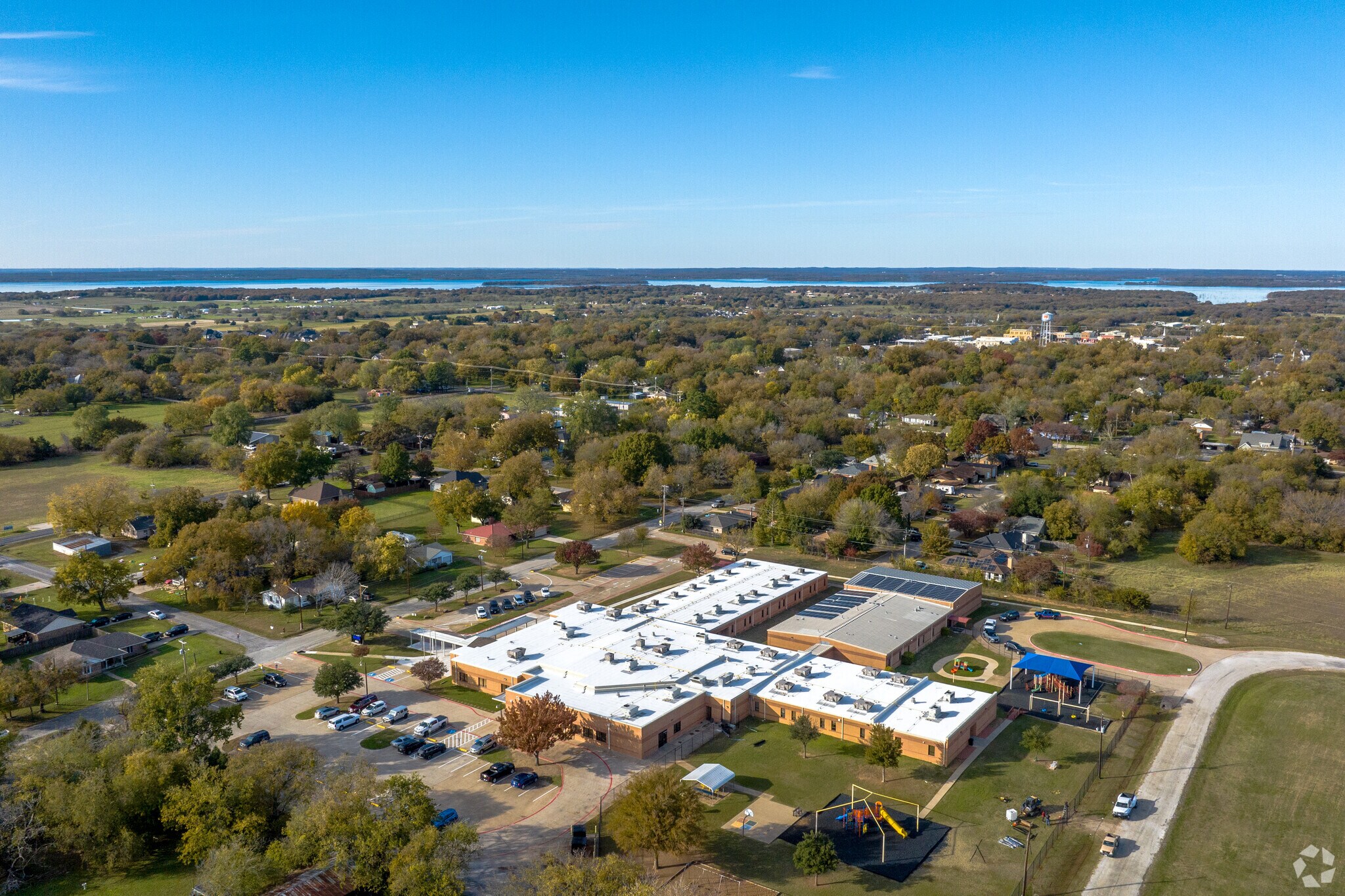 Aerial view of a school building with a playground and surrounding trees under a clear blue sky.