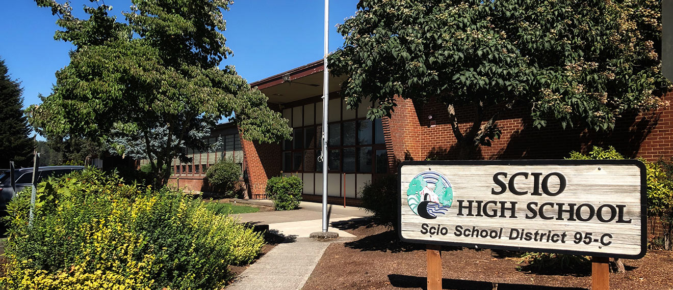A sign reads "SCIO HIGH SCHOOL" in front of a brick building with trees.