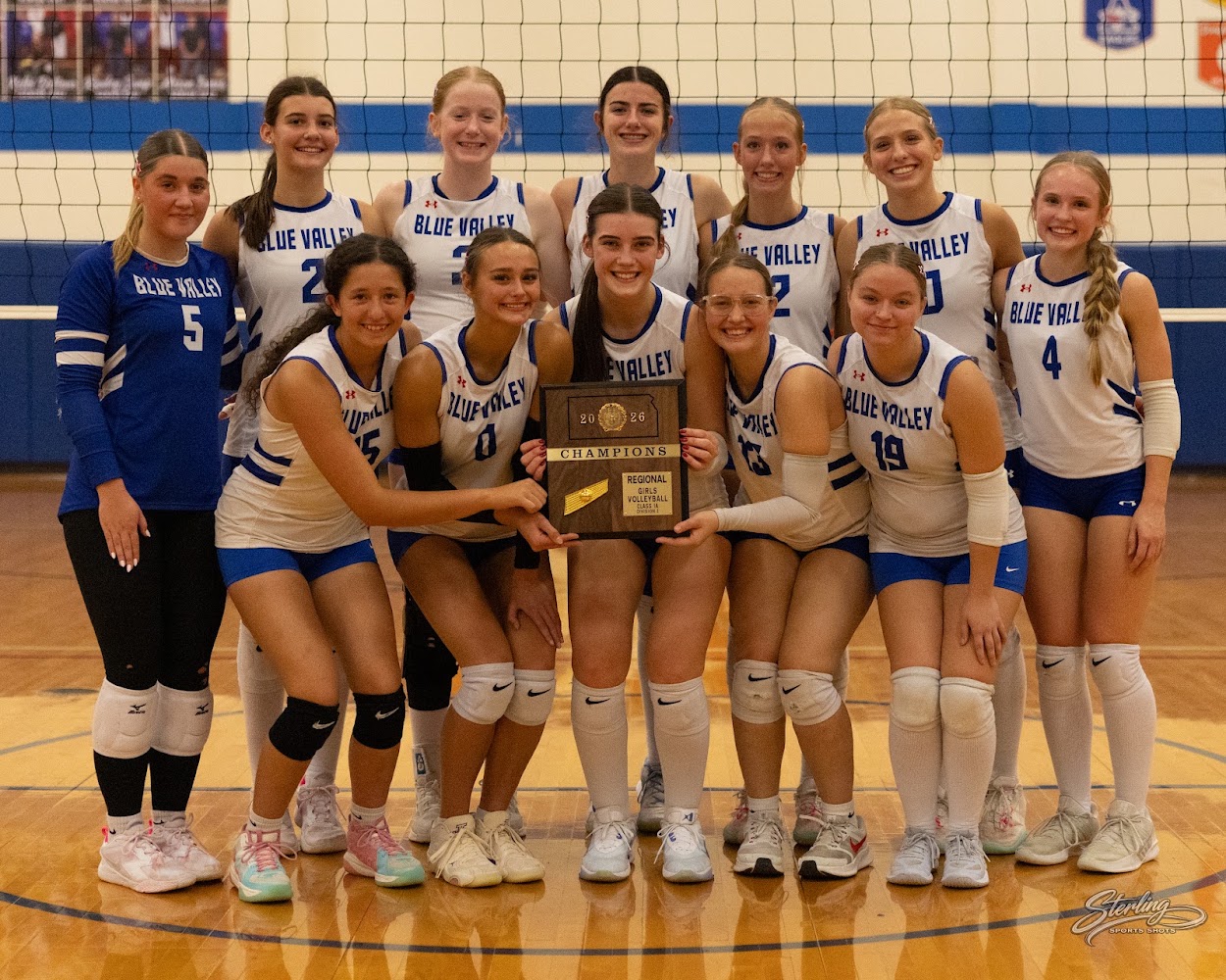 A volleyball team smiles while holding a championship trophy on an indoor court.