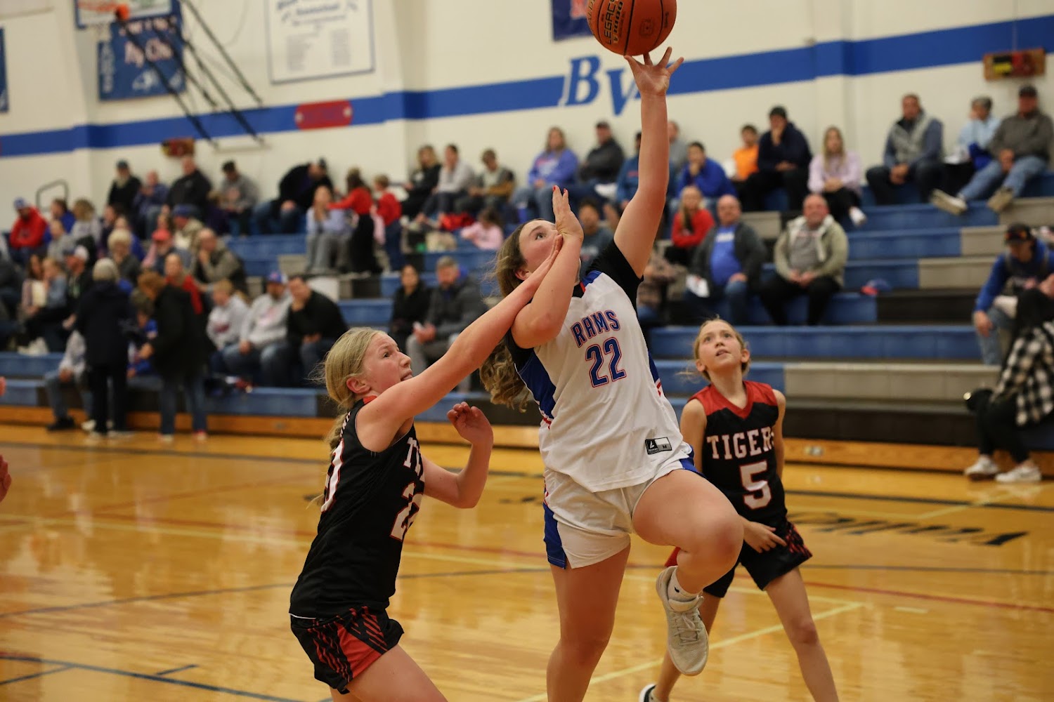A basketball player in a white jersey with the number 22 shoots the ball while defended by an opponent.