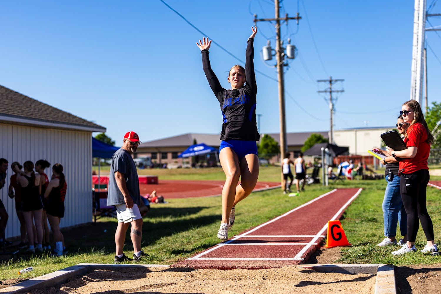 A female athlete leaps during a long jump competition on a sunny day.