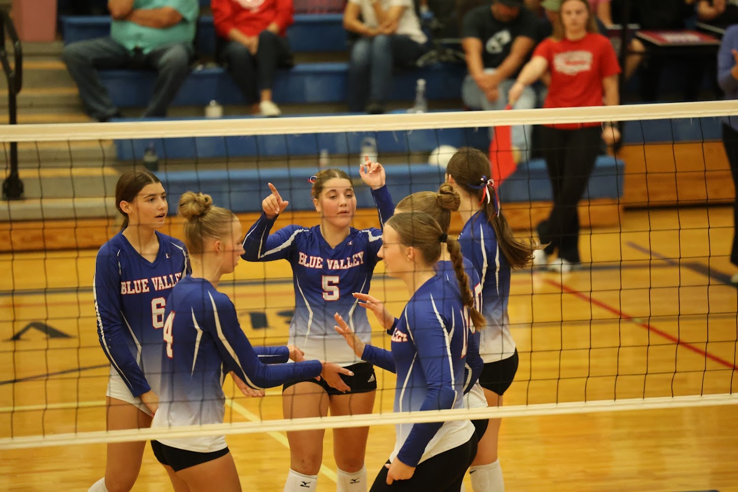 A group of young women in blue and white volleyball uniforms celebrate on a court.