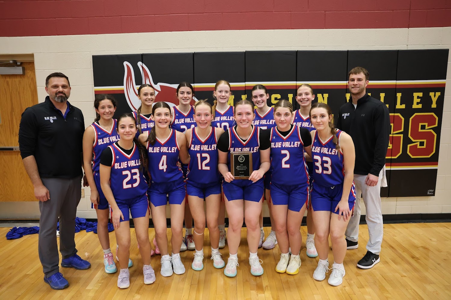 A girls' basketball team poses for a photo with a trophy, wearing purple and white uniforms.
